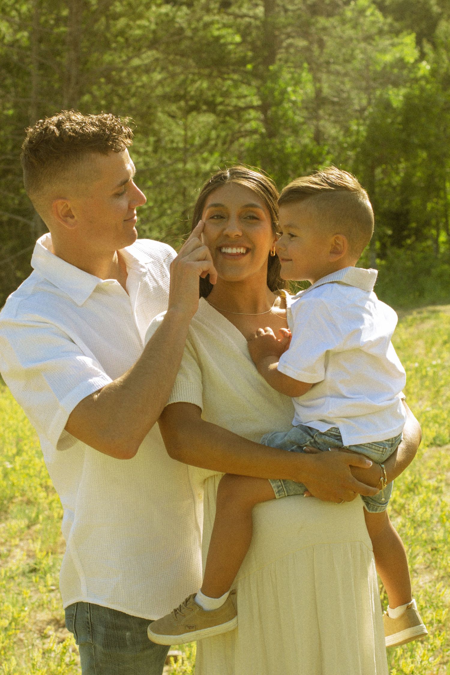 A family shares a joyful moment together outdoors in warm sunlight, wearing coordinated white outfits.