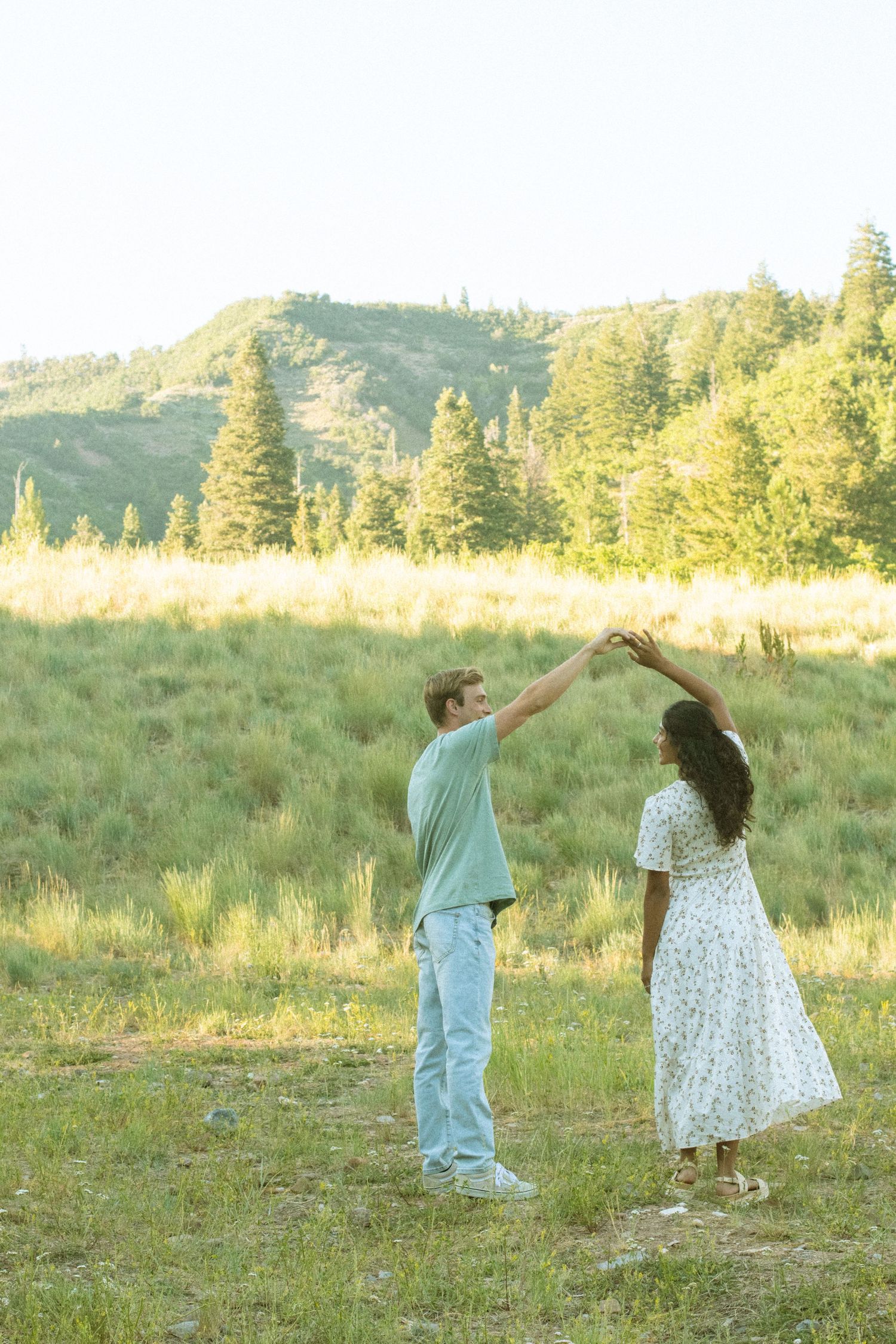 Two young children dance together in a sunlit meadow wearing white and blue outfits during golden hour.