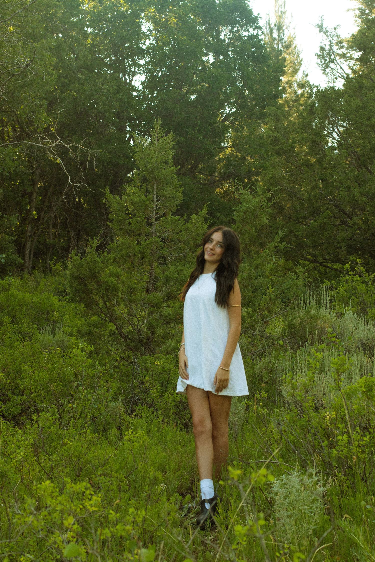 Person in white top enjoying nature in a sunlit meadow with forest backdrop.