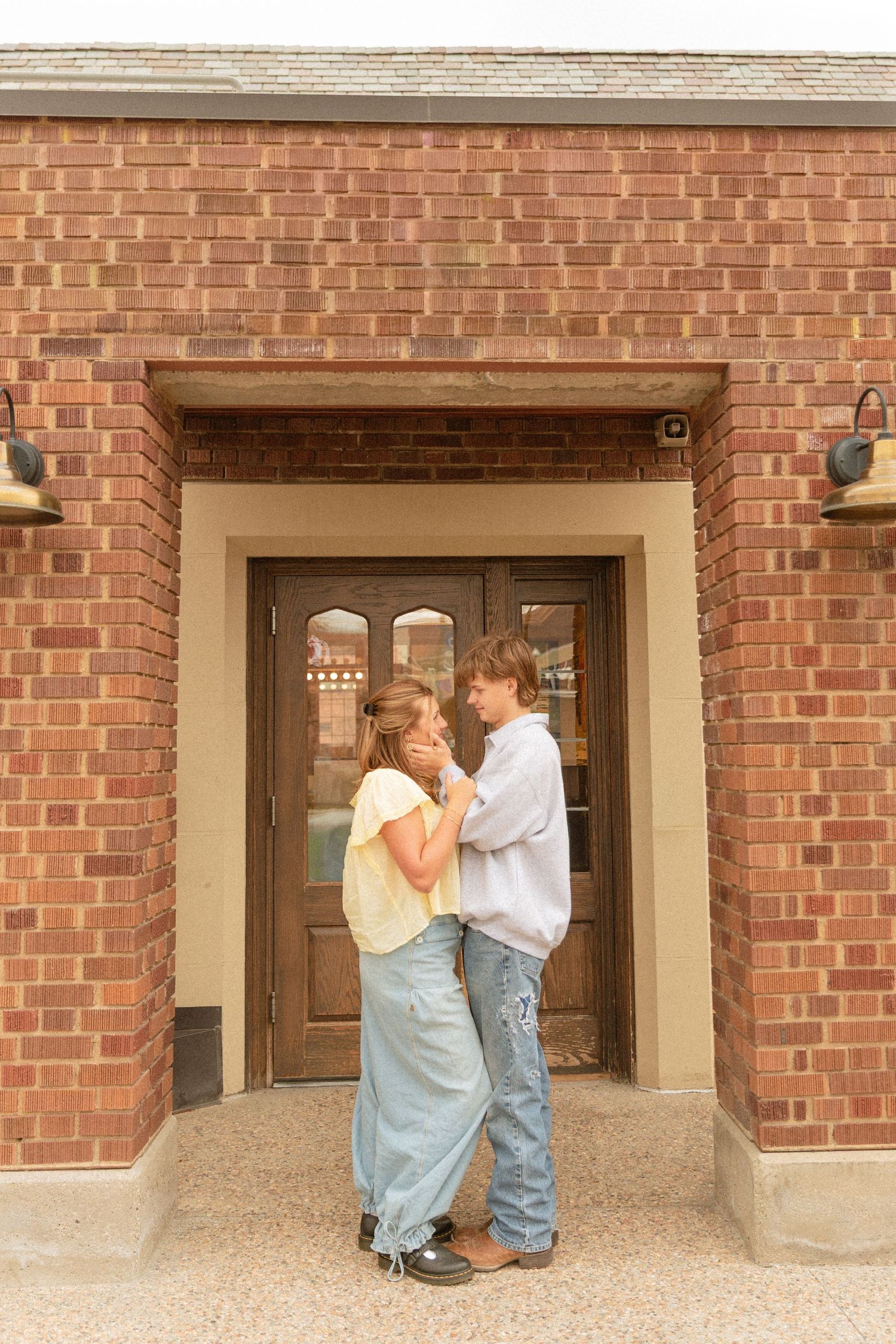 A couple shares an intimate moment while standing in a brick doorway entrance of a traditional building.