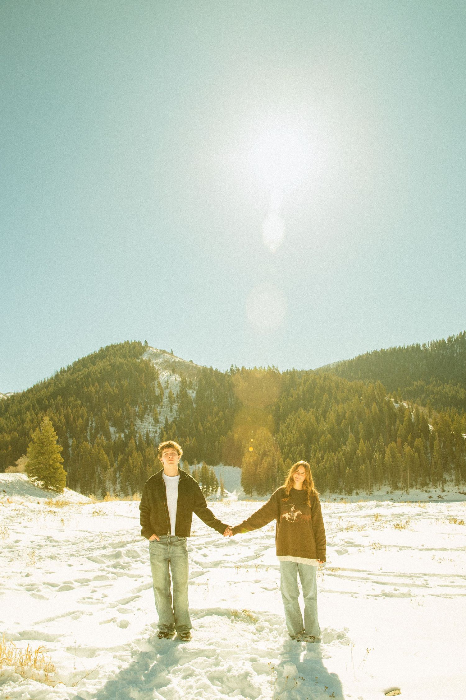 Two friends enjoying a winter day in a snowy mountain landscape with bright sunlight and clear blue skies.