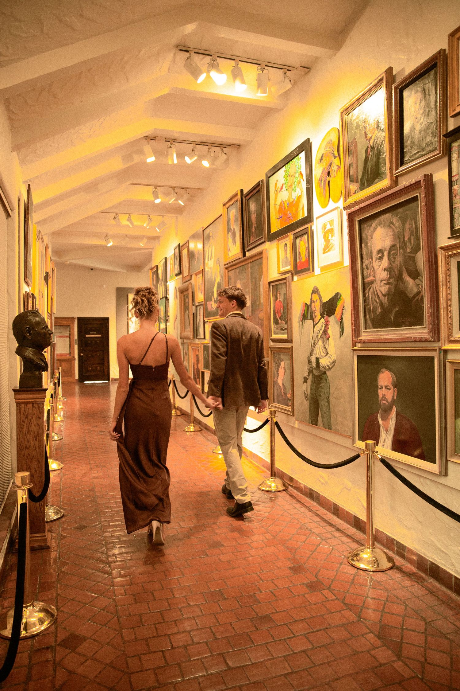Art gallery corridor with brick floor and white walls displaying framed photographs in warm lighting.