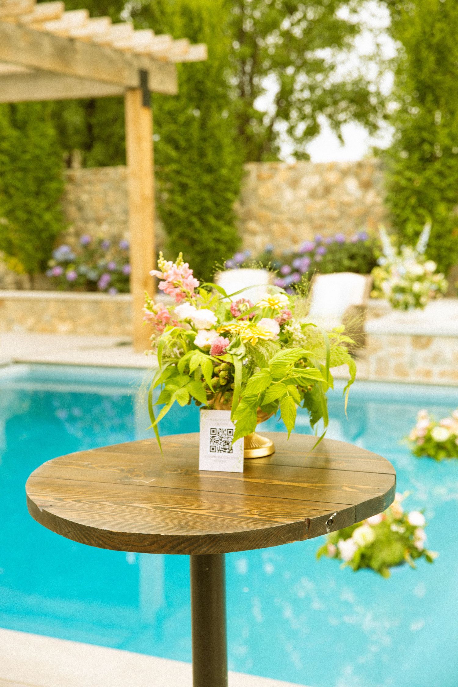 A wooden cocktail table decorated with fresh flowers sits beside a bright blue swimming pool.