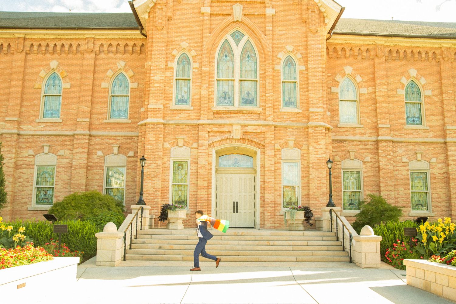 A person jumps with an umbrella on the steps of a historic brick church building with arched windows.