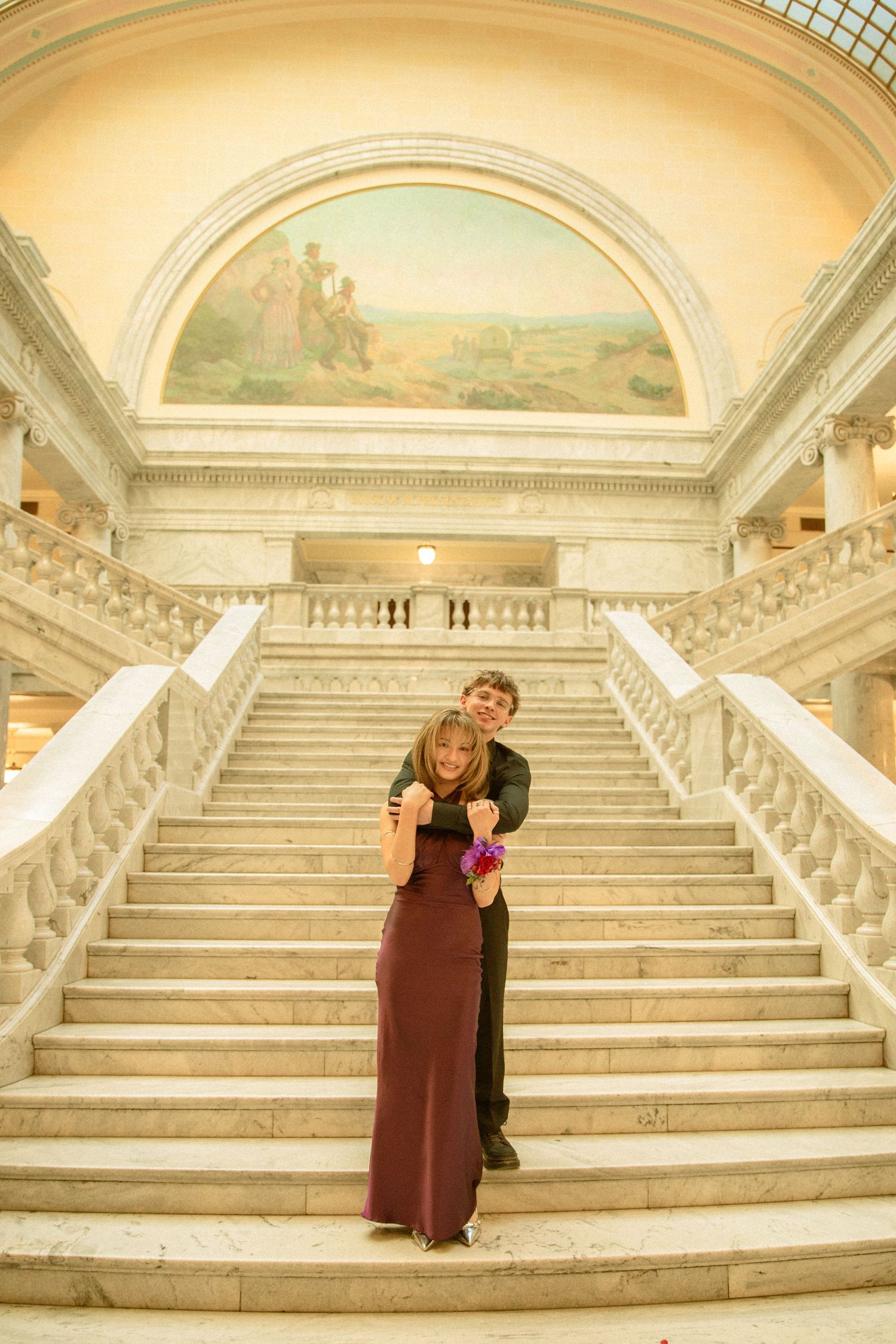 A couple poses on an elegant marble staircase in a grand historic building with arched ceilings and ornate details.
