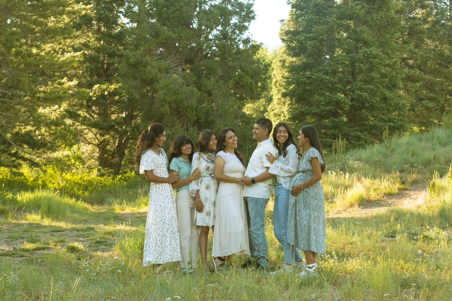 A group gathers for photos in a grassy field surrounded by evergreen trees at sunset.