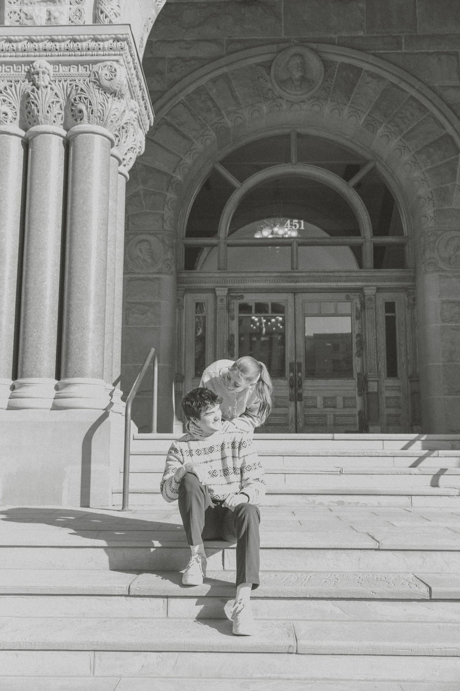 A black and white photo sequence shows two people sitting and interacting on stone steps of a grand building entrance.