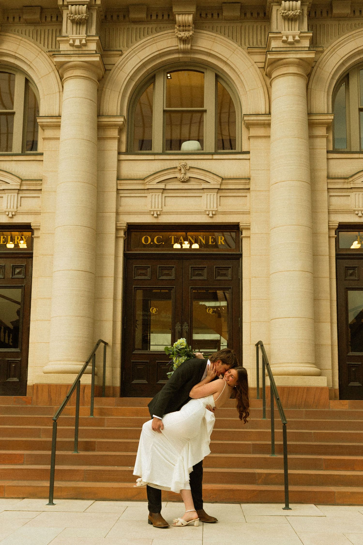 A romantic dip pose on the steps of a grand historic building with elegant stone columns and arched architecture.