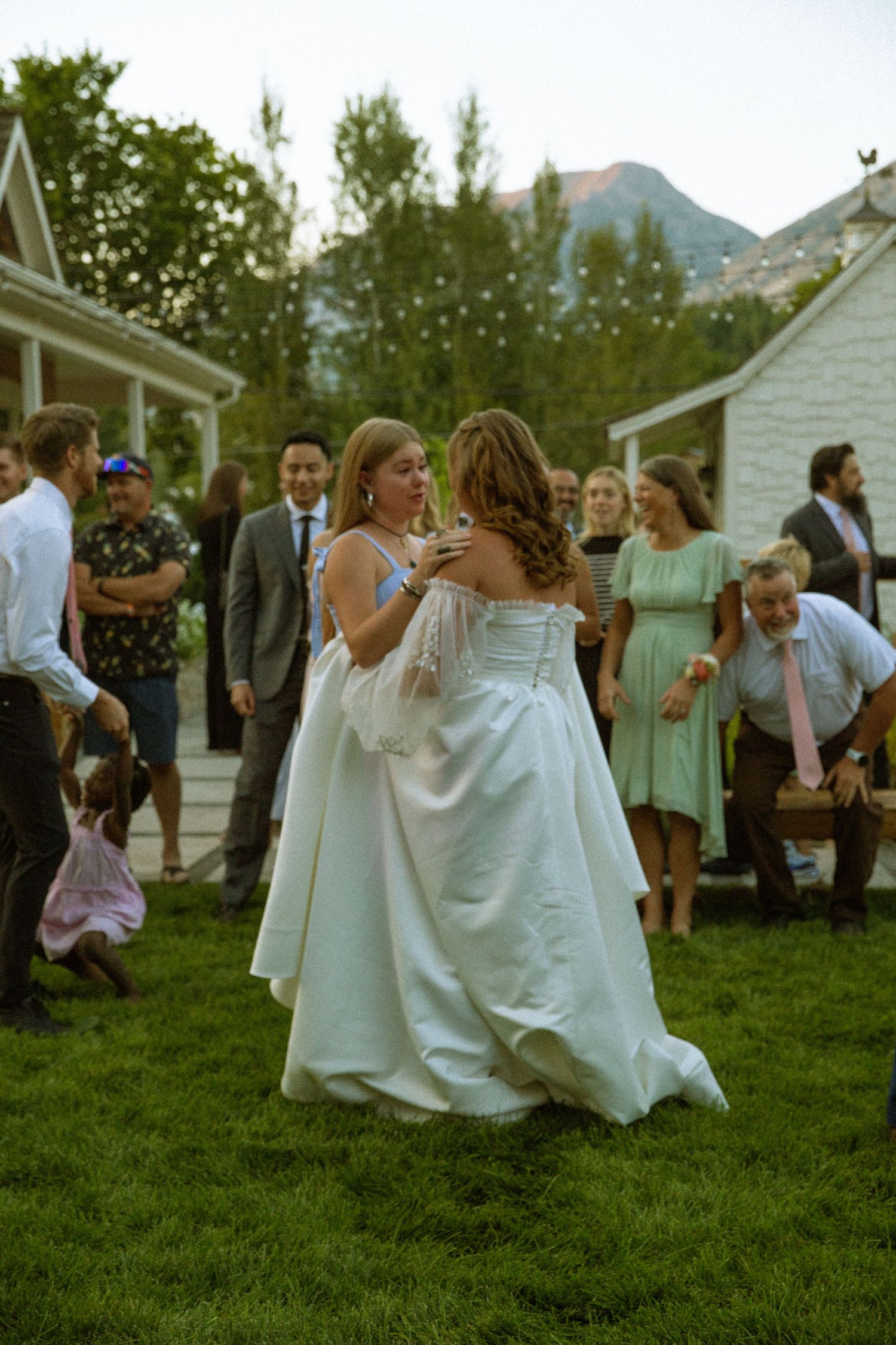 Wedding guests dancing and celebrating on a grassy lawn with mountain views.
