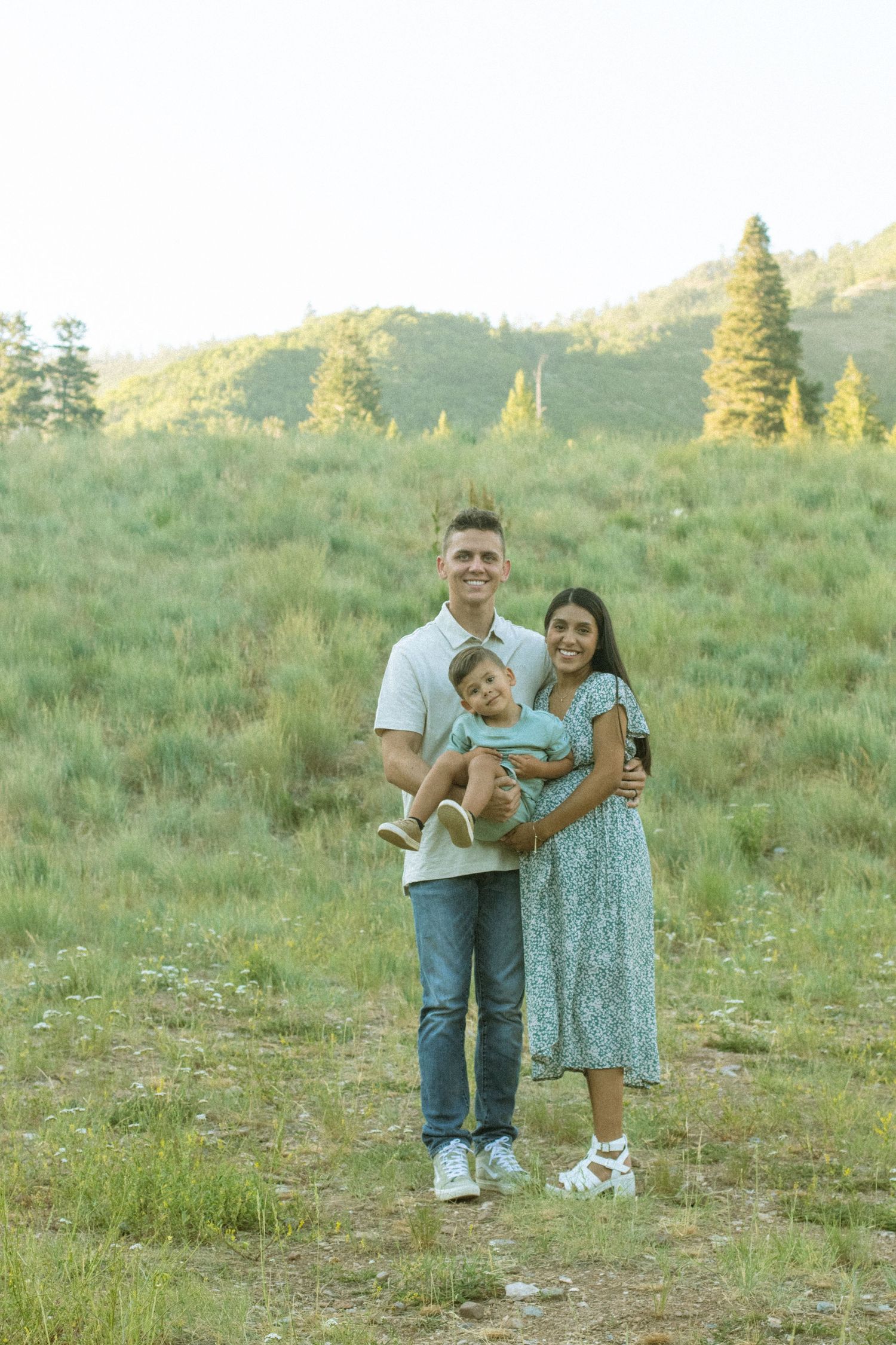 A family shares joyful moments together in a sunlit grassy meadow during a summer photoshoot.