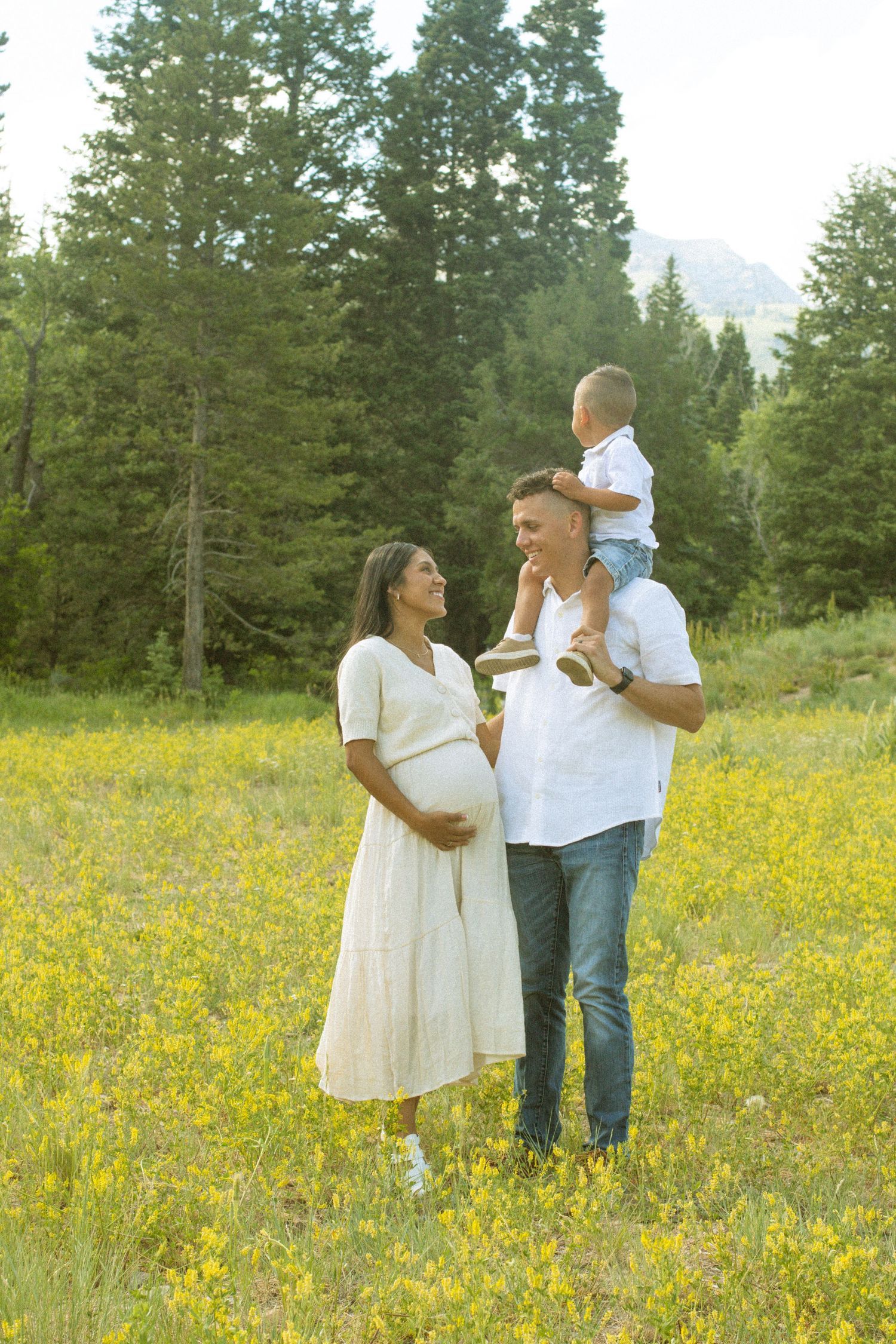 A couple stands together in a sunny meadow filled with yellow wildflowers as their white clothing catches the breeze.