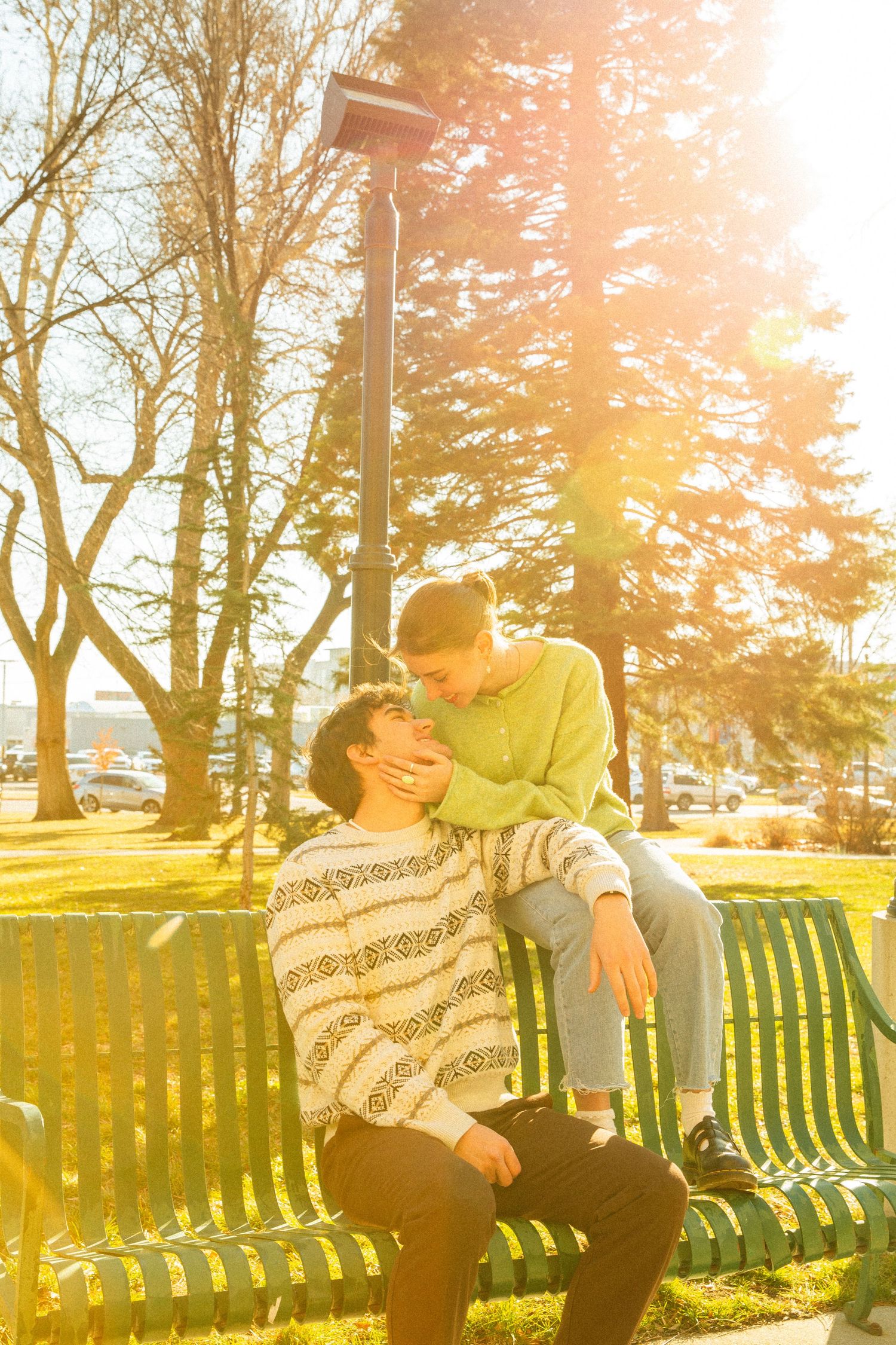 A couple shares a tender moment on a park bench at sunset with golden sunlight streaming through the trees.