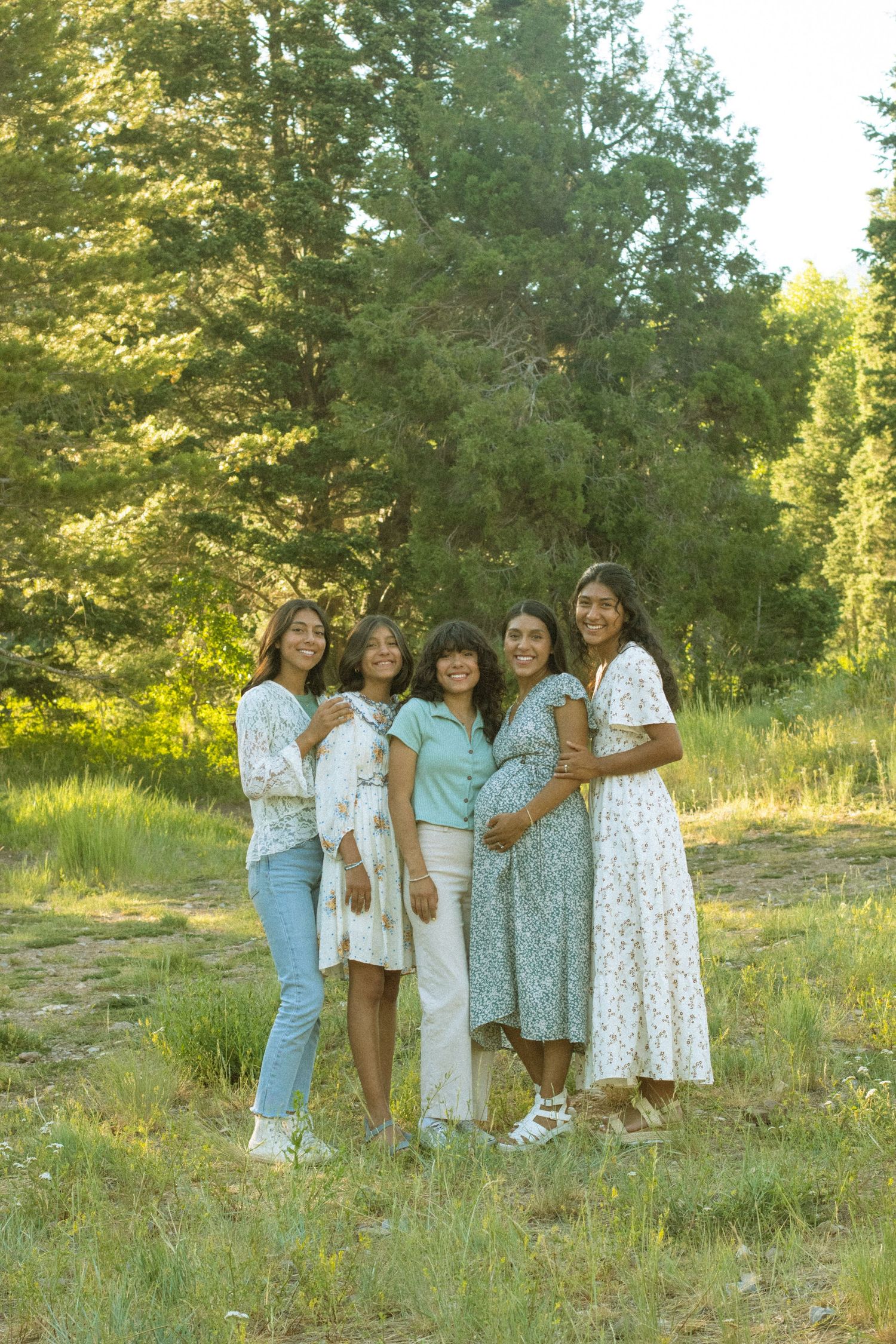 A group in coordinated white and blue outfits poses together on a grassy hillside during golden hour.