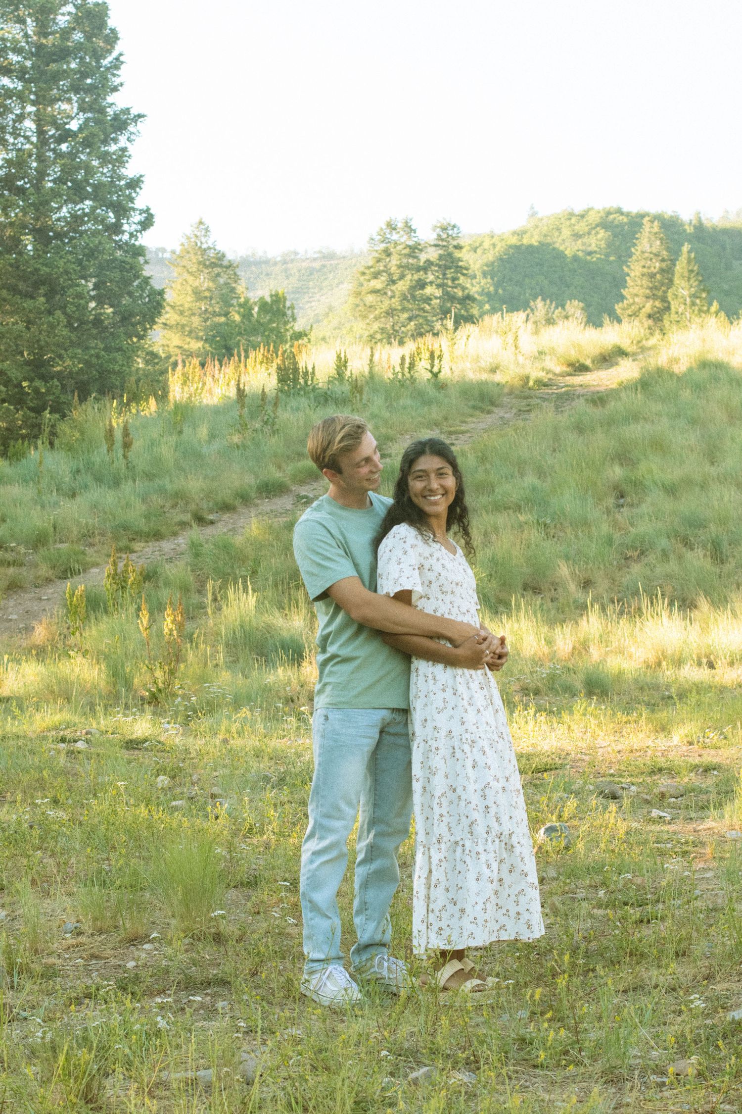 A couple embraces in a sunlit meadow during a romantic outdoor photo session.