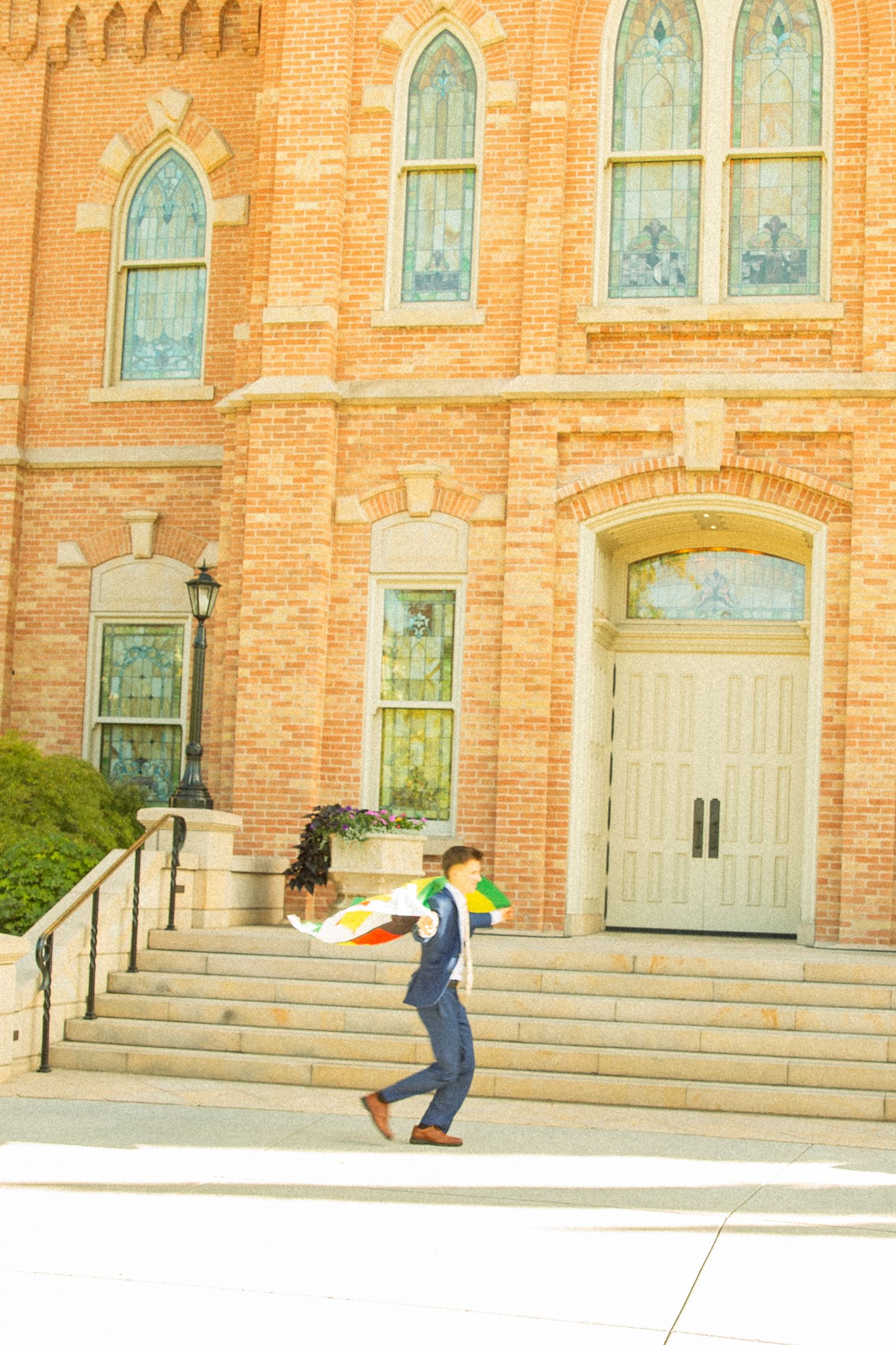 Skateboarder performing a trick in front of a historic brick church building with stained glass windows.