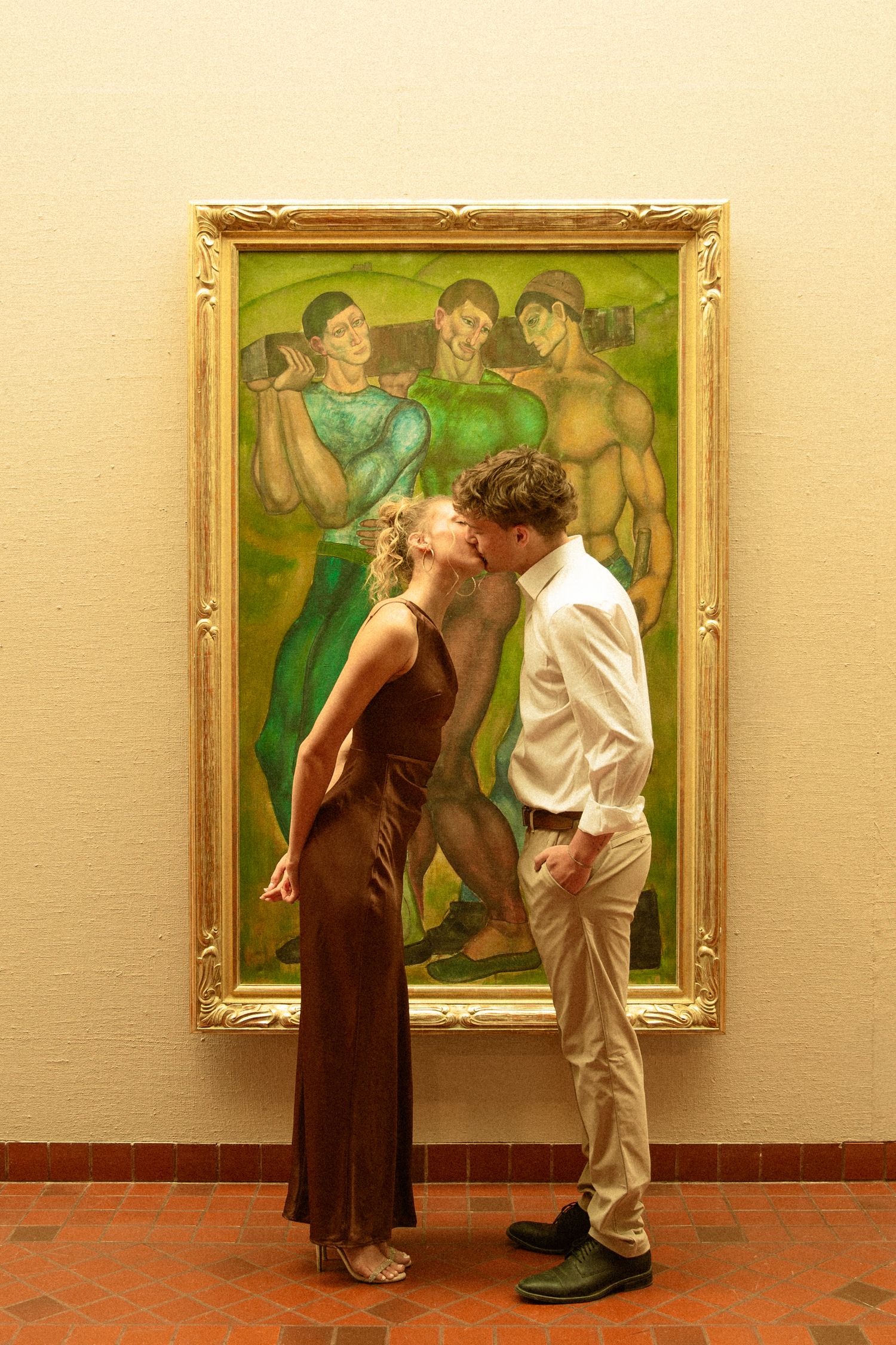 A couple mimics a romantic scene depicted in a classical painting hanging on a museum wall.