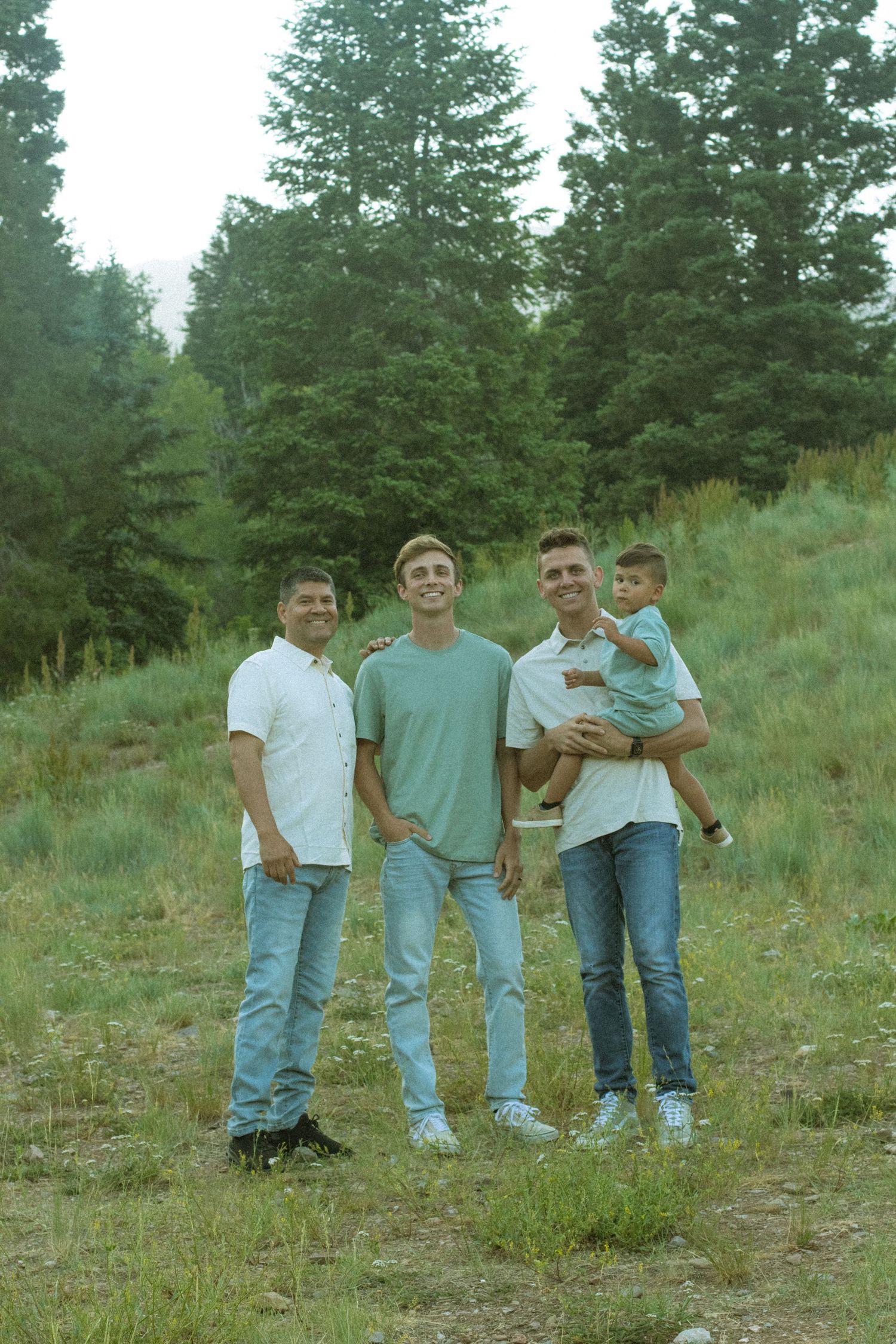 A group stands together on a grassy hillside with evergreen trees in the background.
