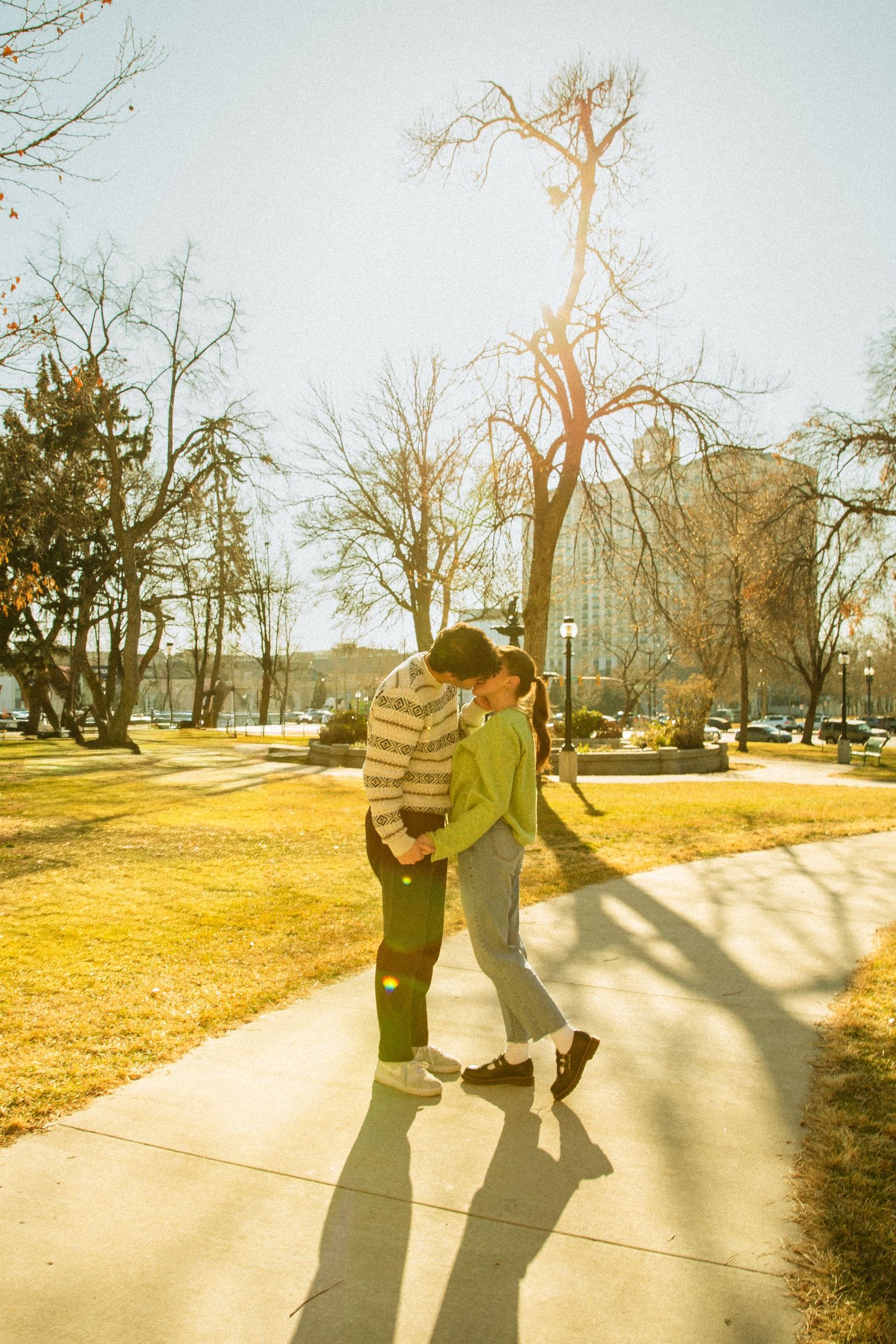 A couple casts long shadows while walking together on a sunlit path during golden hour.
