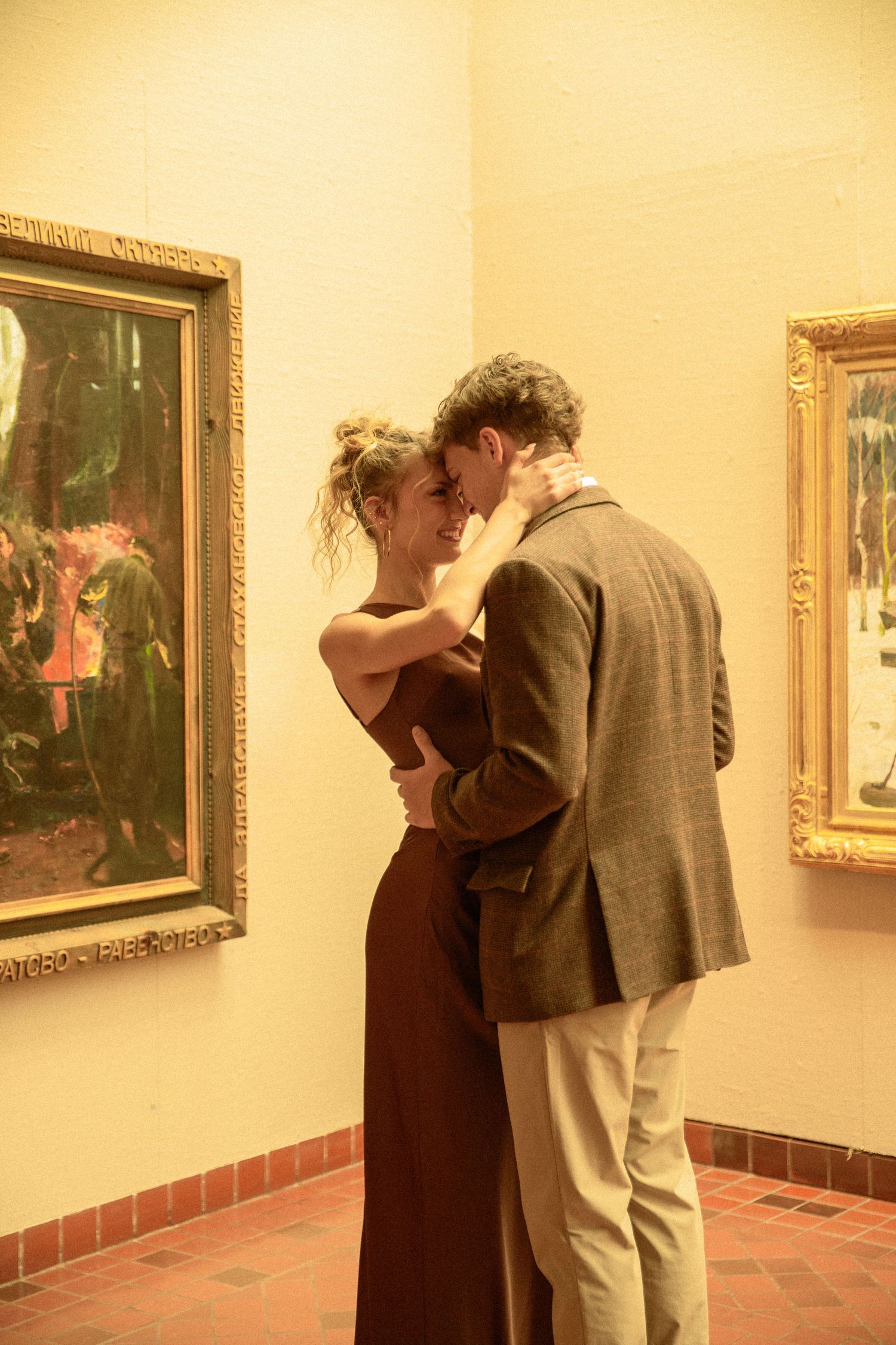 Two people viewing artwork in a museum gallery with framed paintings hanging on cream colored walls.