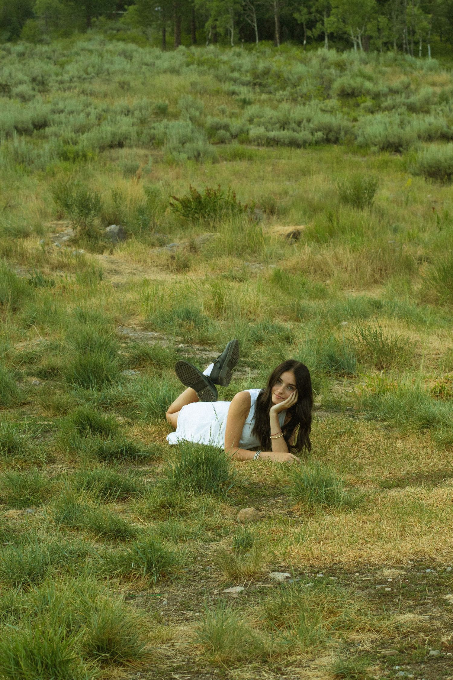 A person lies peacefully in a grassy meadow surrounded by lush green trees and vegetation.