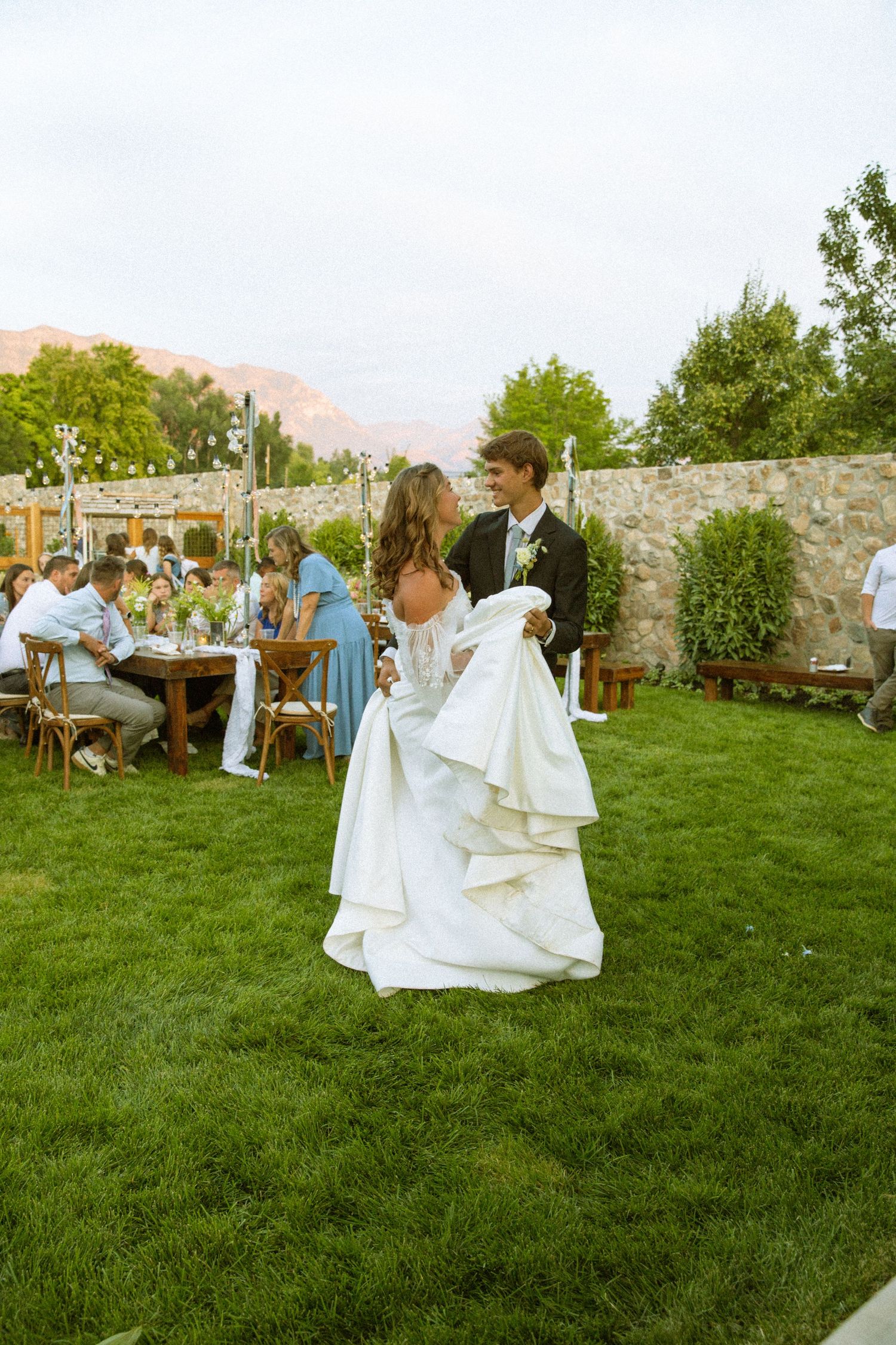 Guests mingle on a manicured lawn at an elegant outdoor wedding reception with stone walls.
