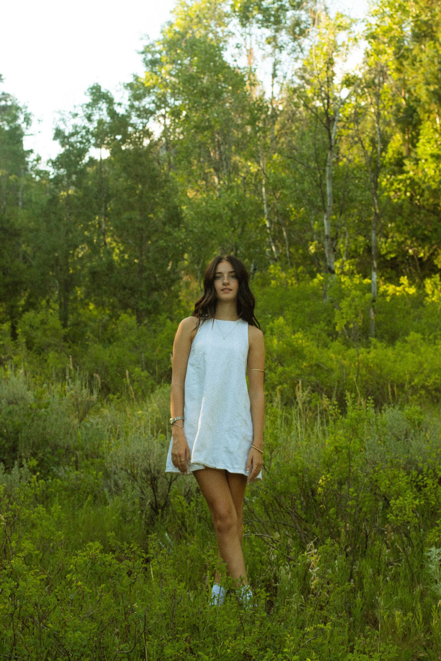 A figure stands in a lush green field surrounded by trees during golden hour lighting.
