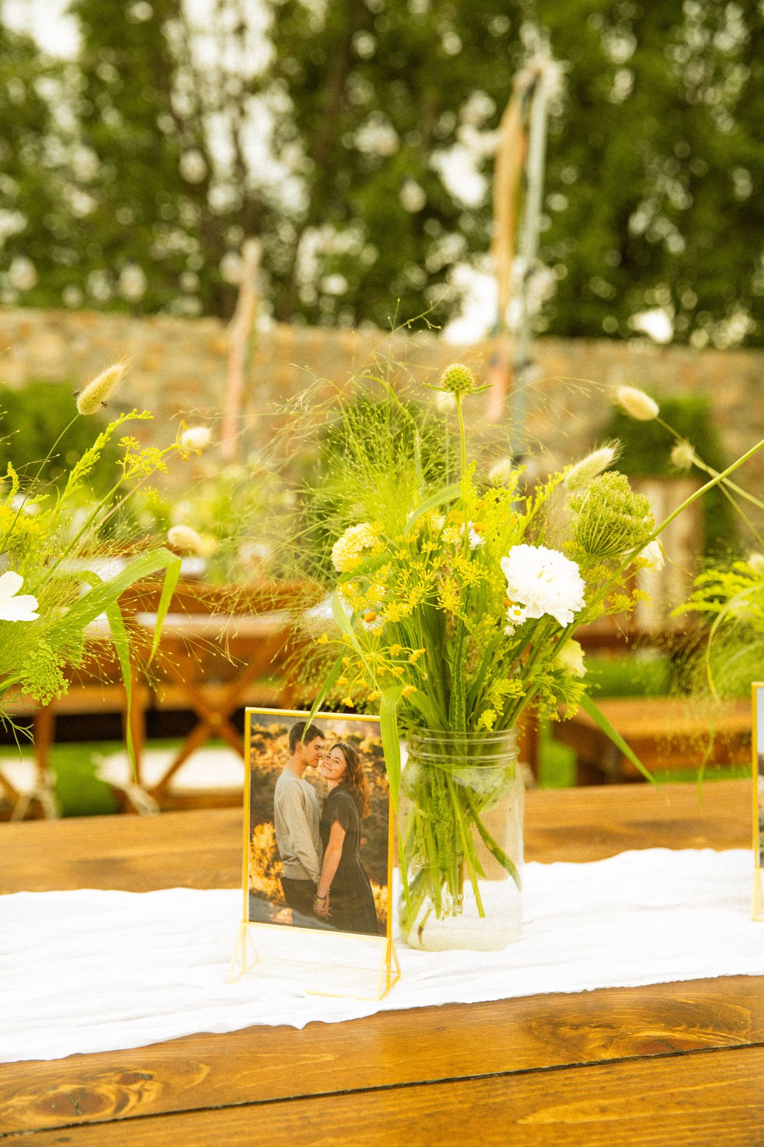 Rustic wooden table decorated with delicate floral centerpieces and greenery for an outdoor event.
