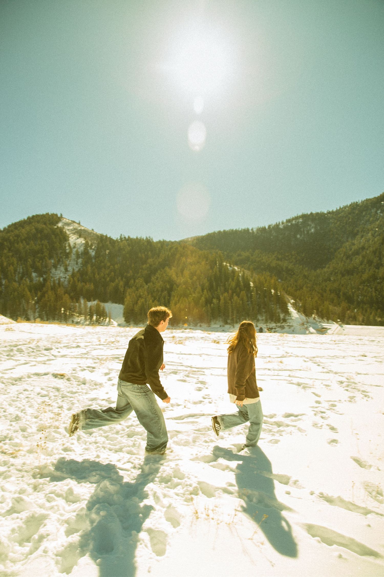 Two people play in deep snow on a sunny winter day with mountains in the background.