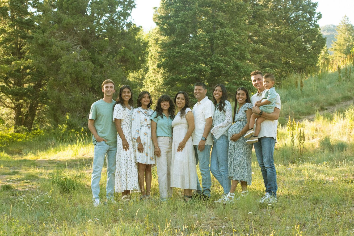 A group wearing coordinated blue and white outfits poses together on a grassy hillside during golden hour.