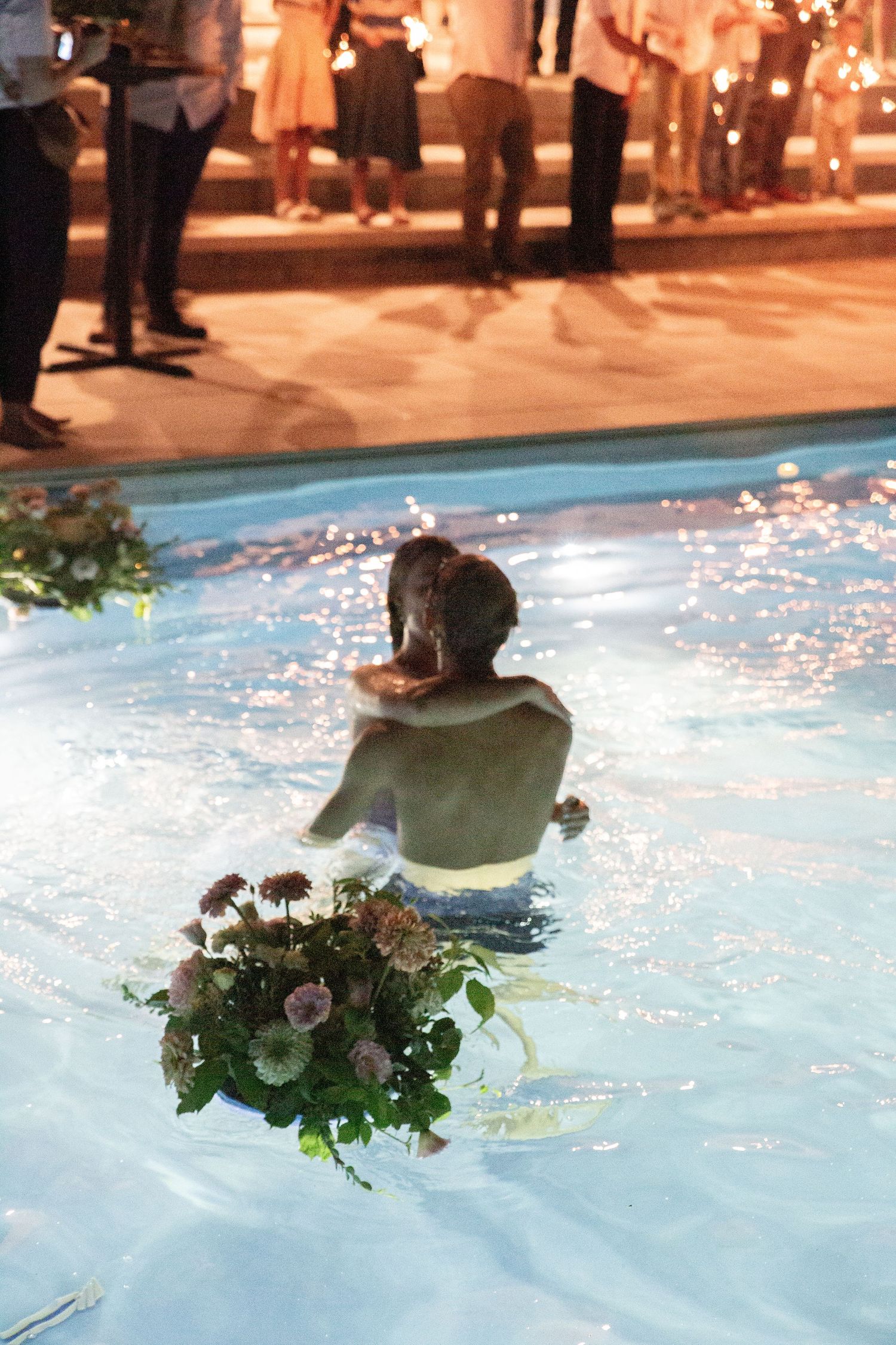 Underwater photo showing flowers and fabric floating in illuminated blue pool water.