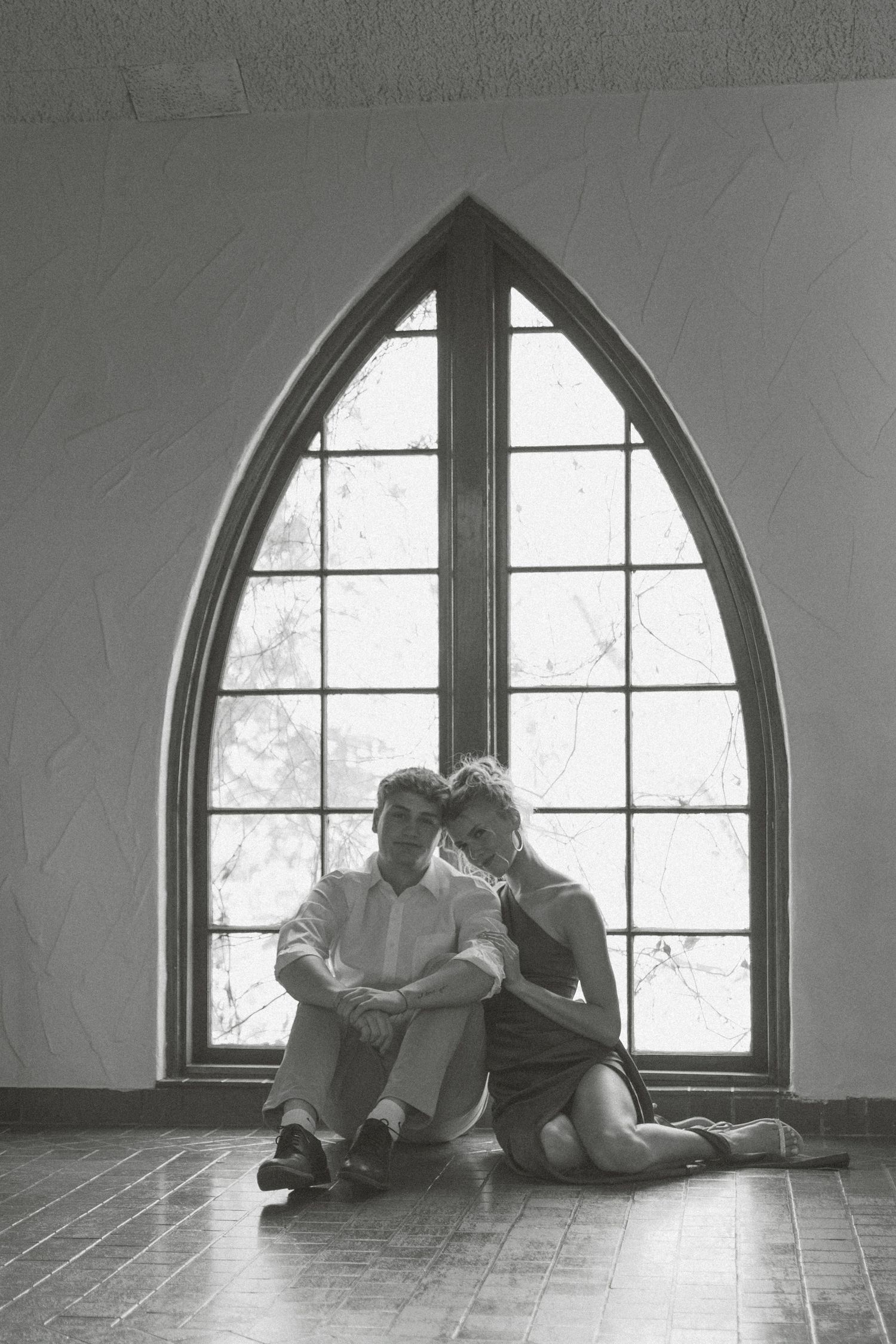 Two people sit together reading books by a large arched window in a minimalist black and white photo sequence.