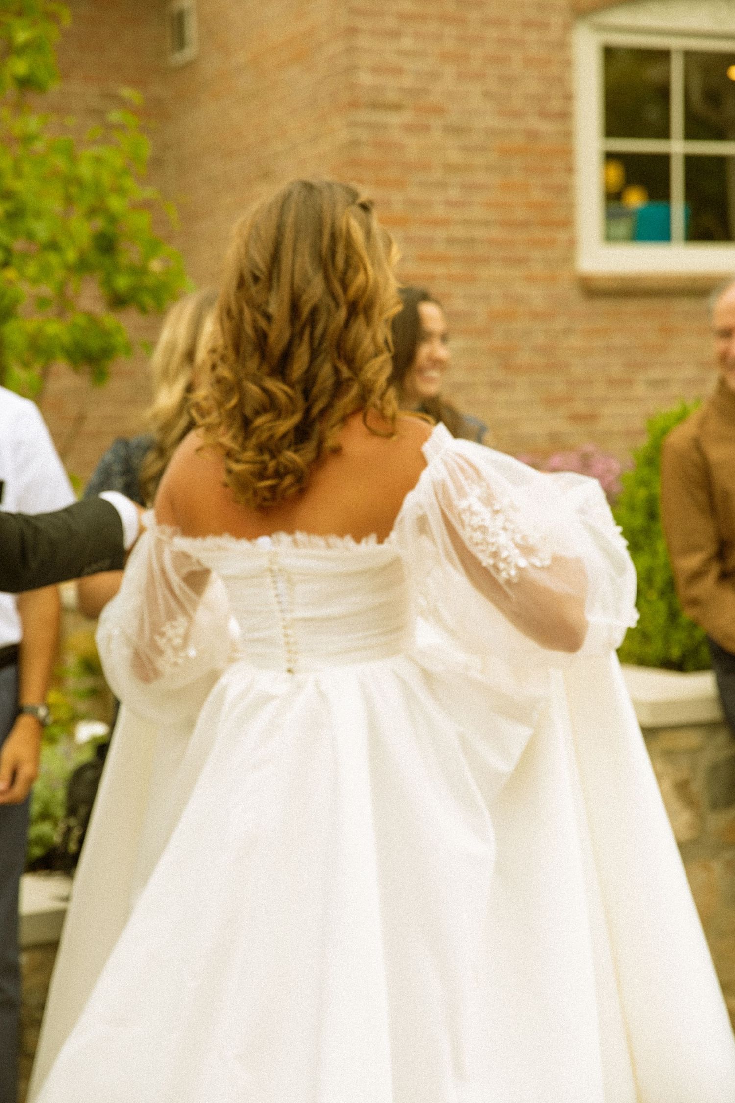 Back view of bride's white wedding dress with delicate lace details against brick wall.