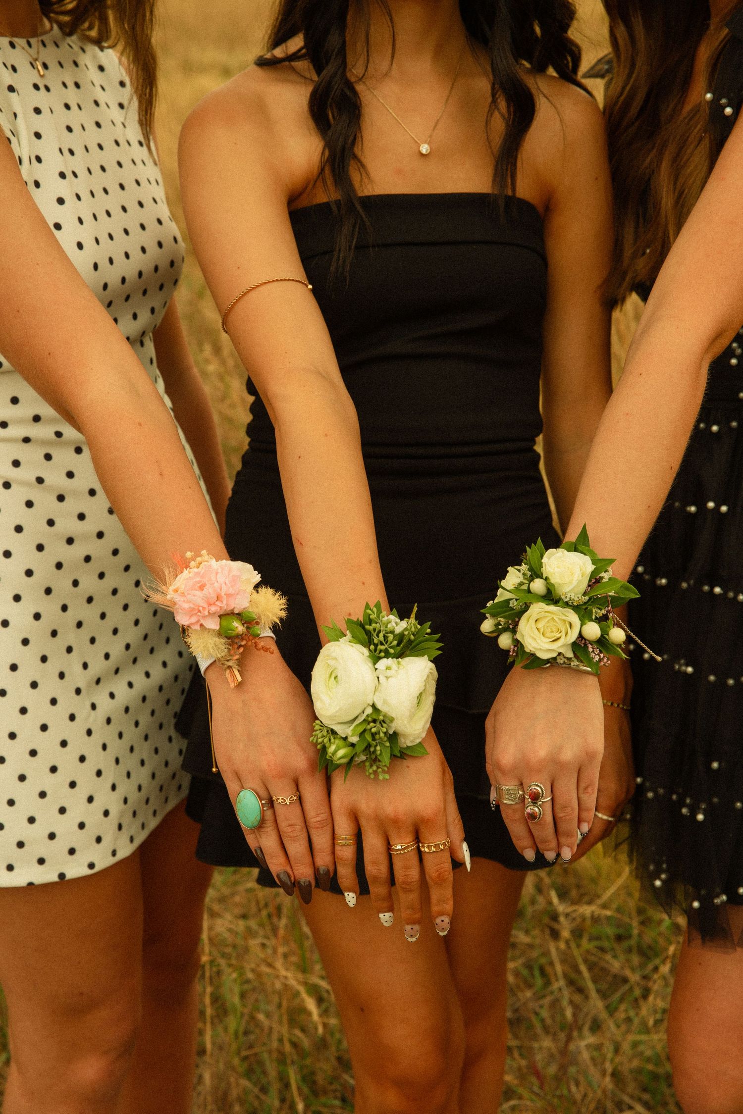 Three people wearing corsages display their wrists together showing delicate floral arrangements in pink and white.