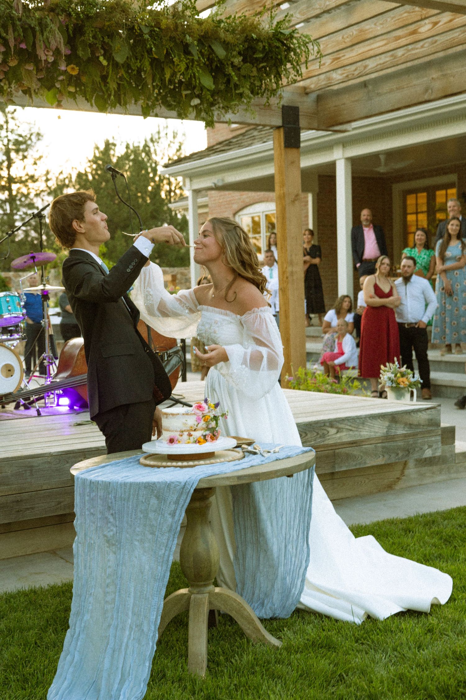 A wedding couple shares a playful cake-smashing moment at their outdoor reception.