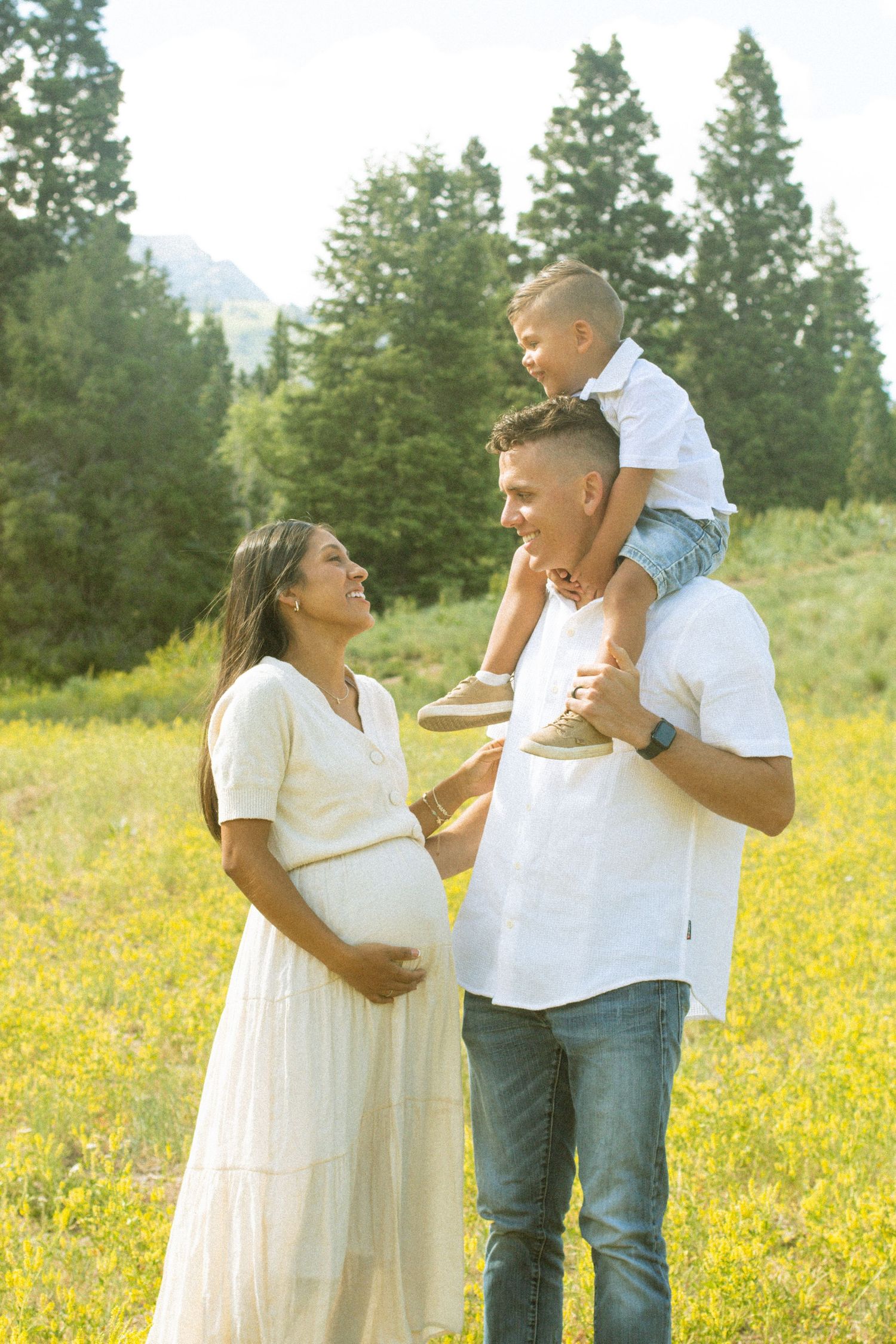 A couple shares joyful moments in a field of yellow wildflowers with evergreen trees in the background.