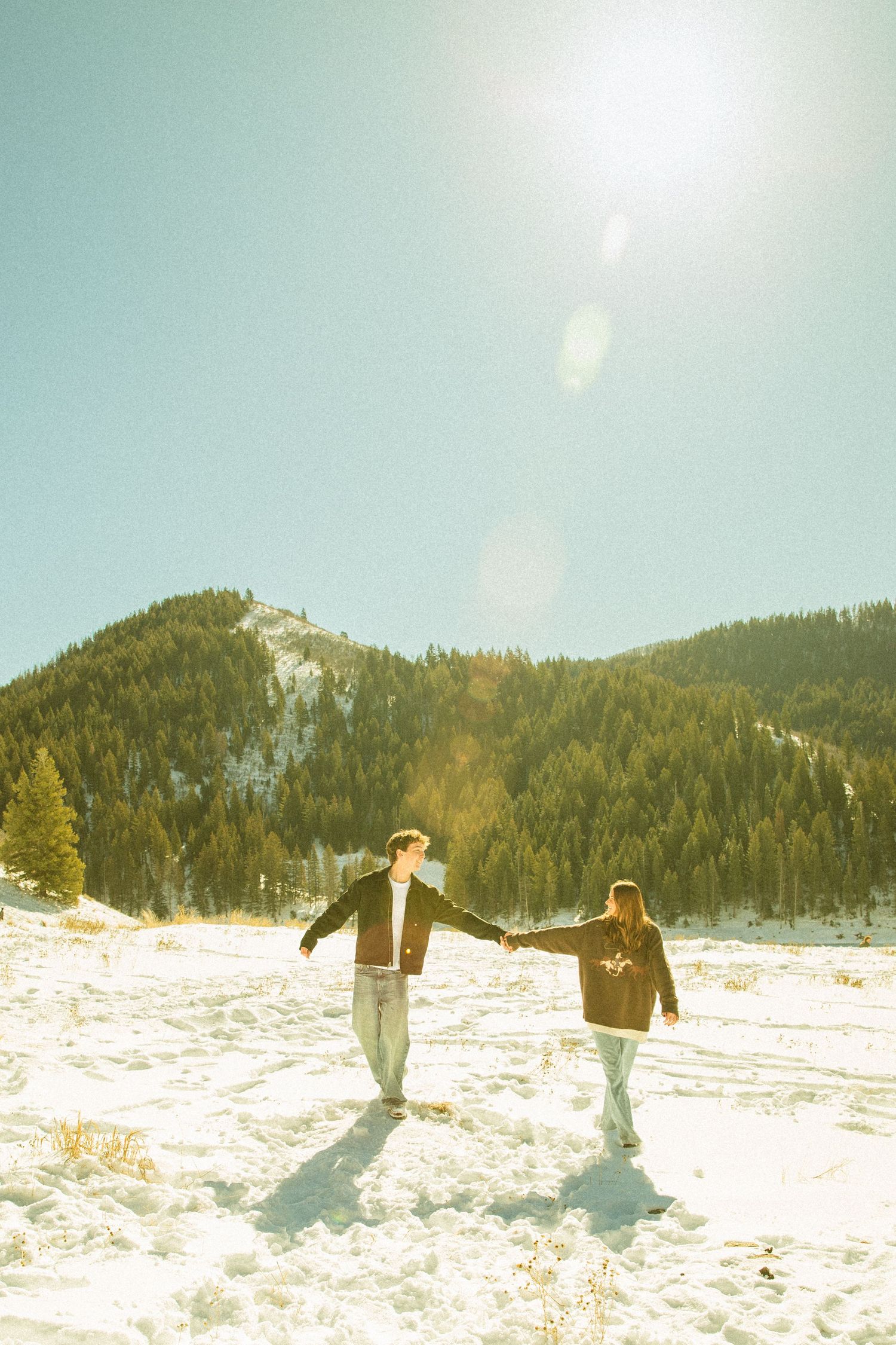 Three people spread their arms wide while standing in deep snow on a sunny winter mountain slope.