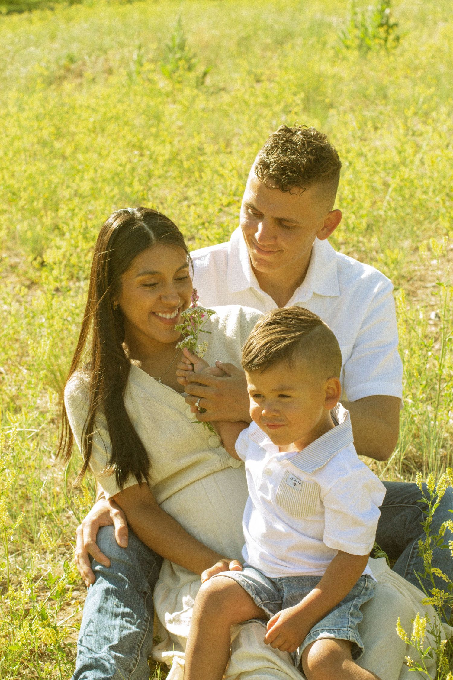 A family sits together in a grassy field on a sunny day, sharing joyful moments and laughter together.