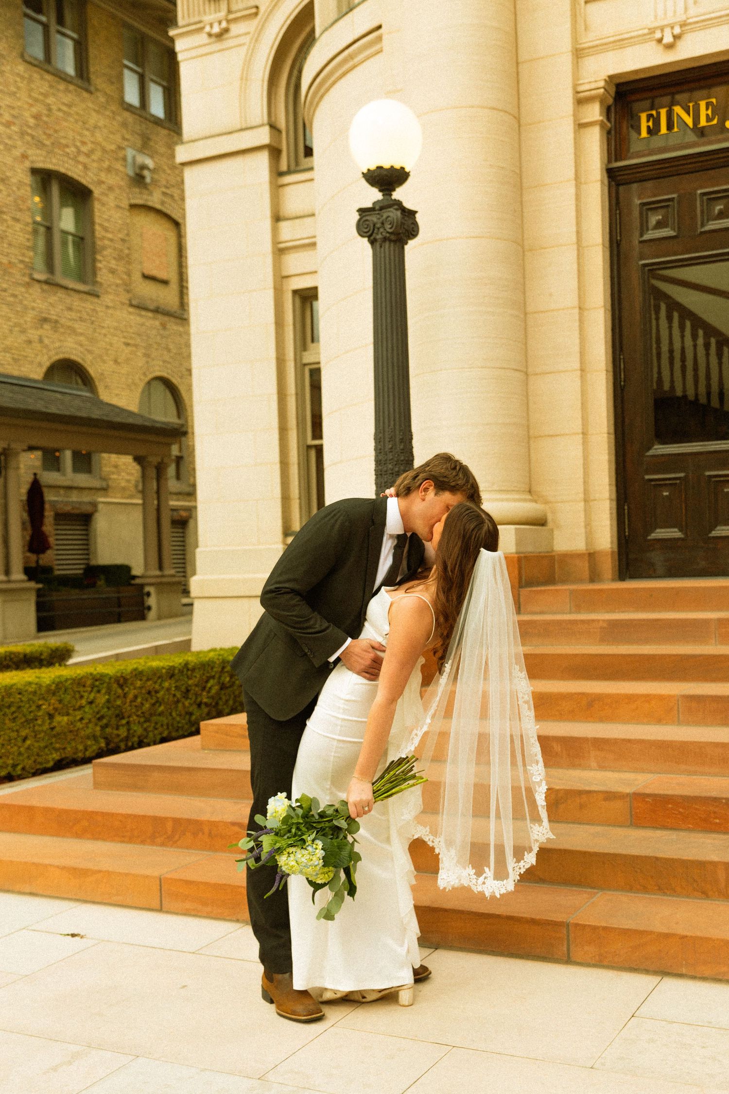 A romantic wedding moment on the steps of an elegant stone building with classical columns and architecture.