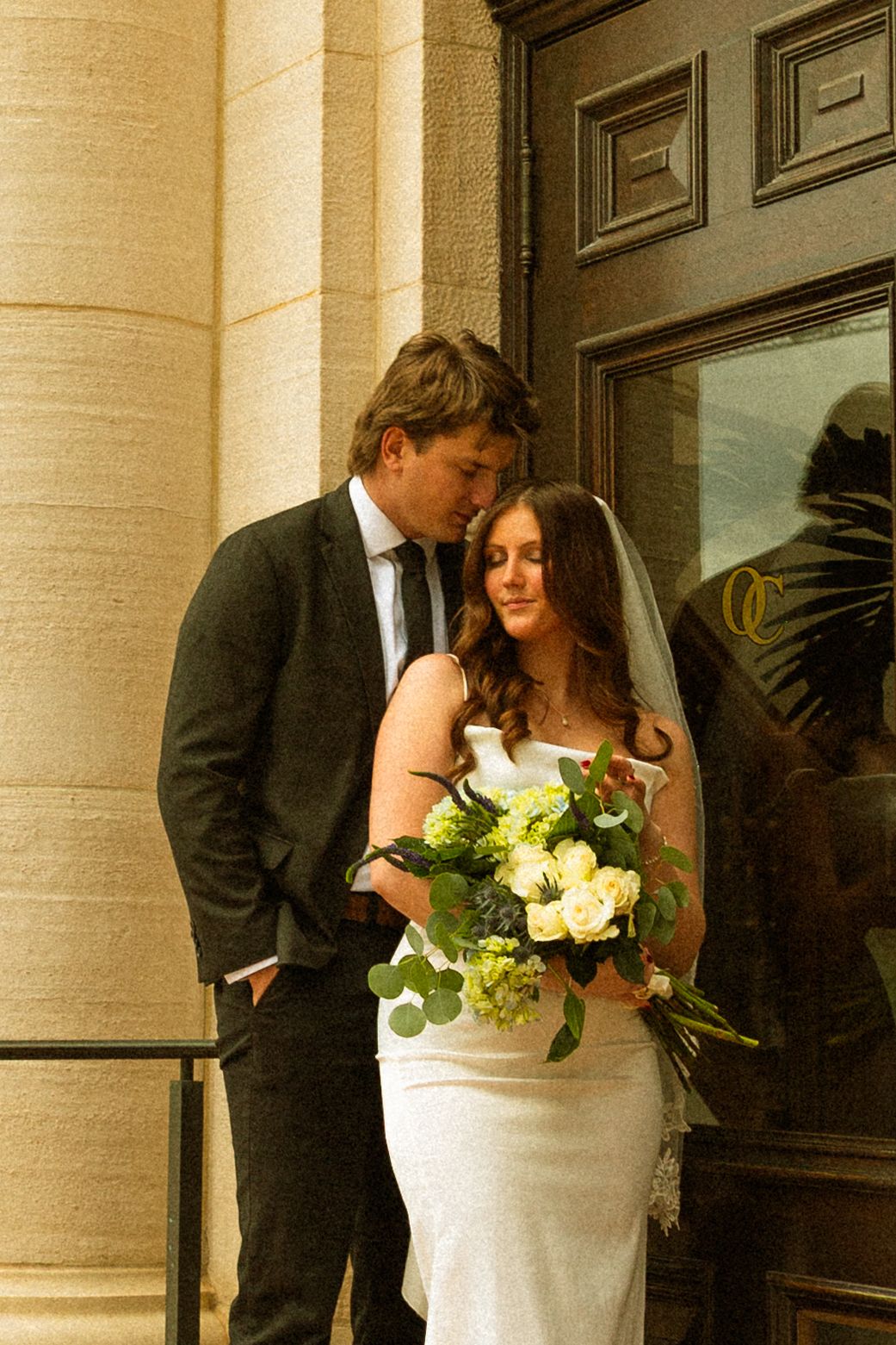 A romantic wedding moment captured on an elegant porch with white columns and yellow floral arrangements.