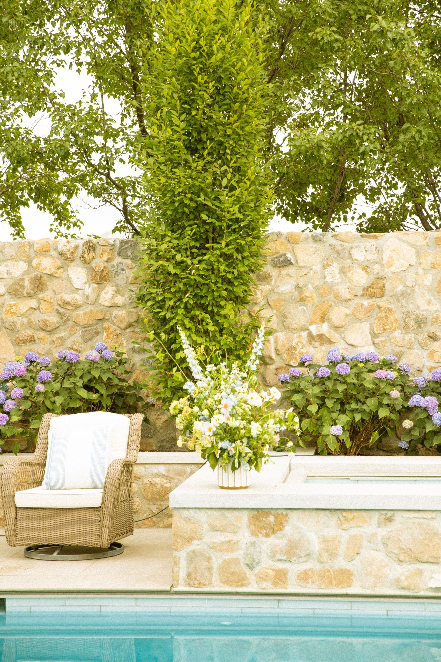 A tranquil poolside setting with stone walls, lounge chairs, and lush greenery creating a relaxing outdoor oasis.