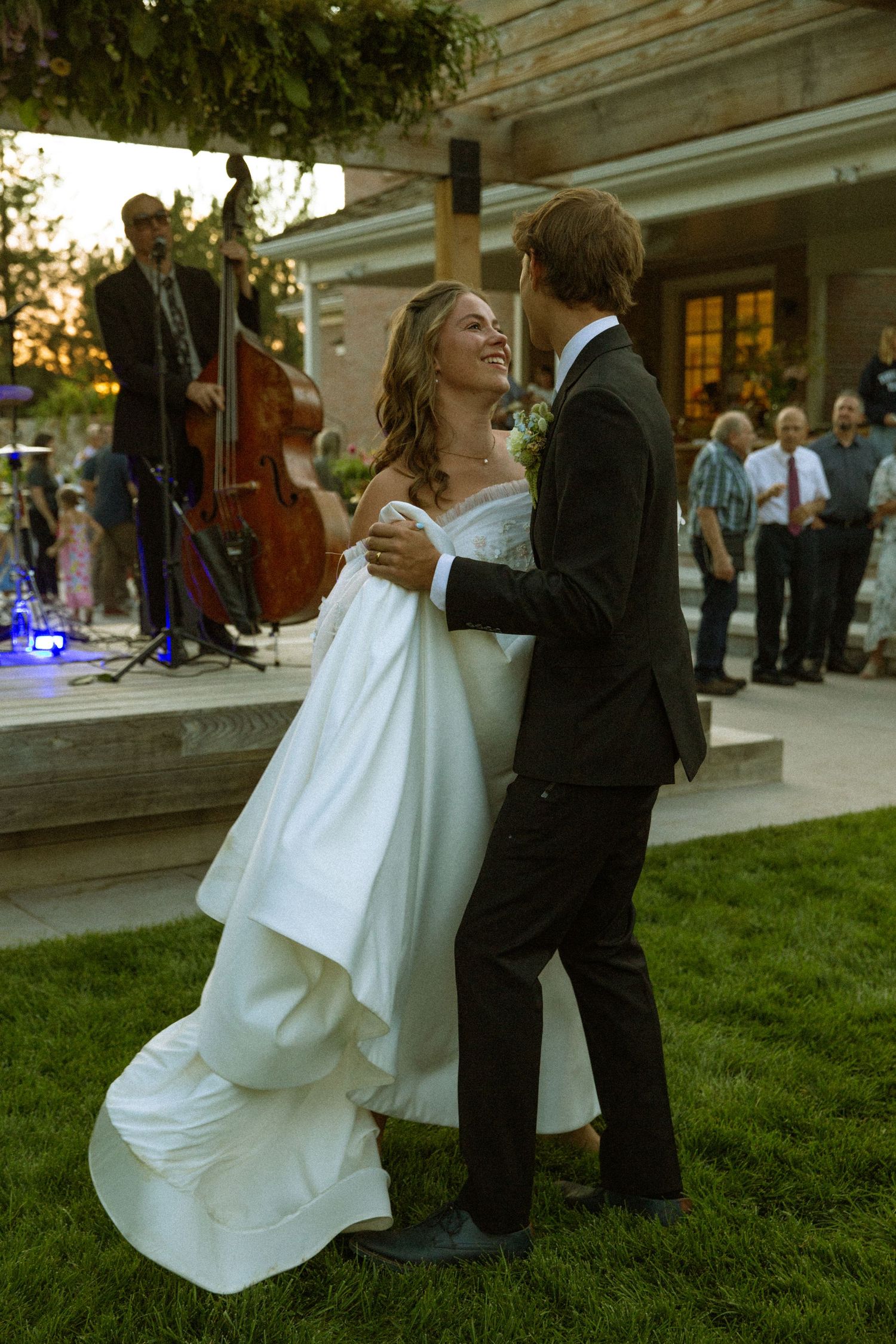A couple dances on grass during a wedding reception, with the bride's white dress flowing gracefully.