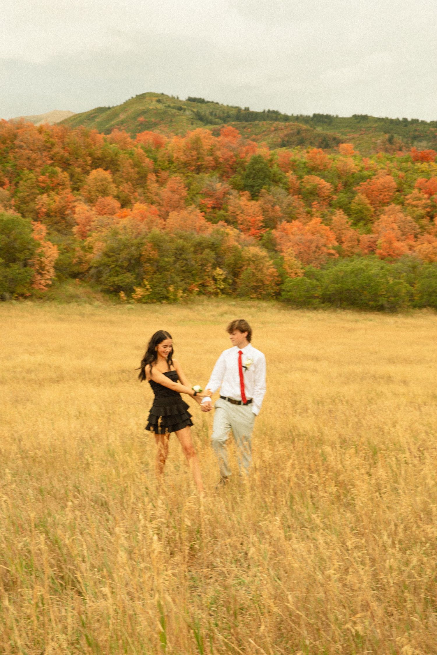 A couple dances in a golden field with autumn trees creating a colorful backdrop.