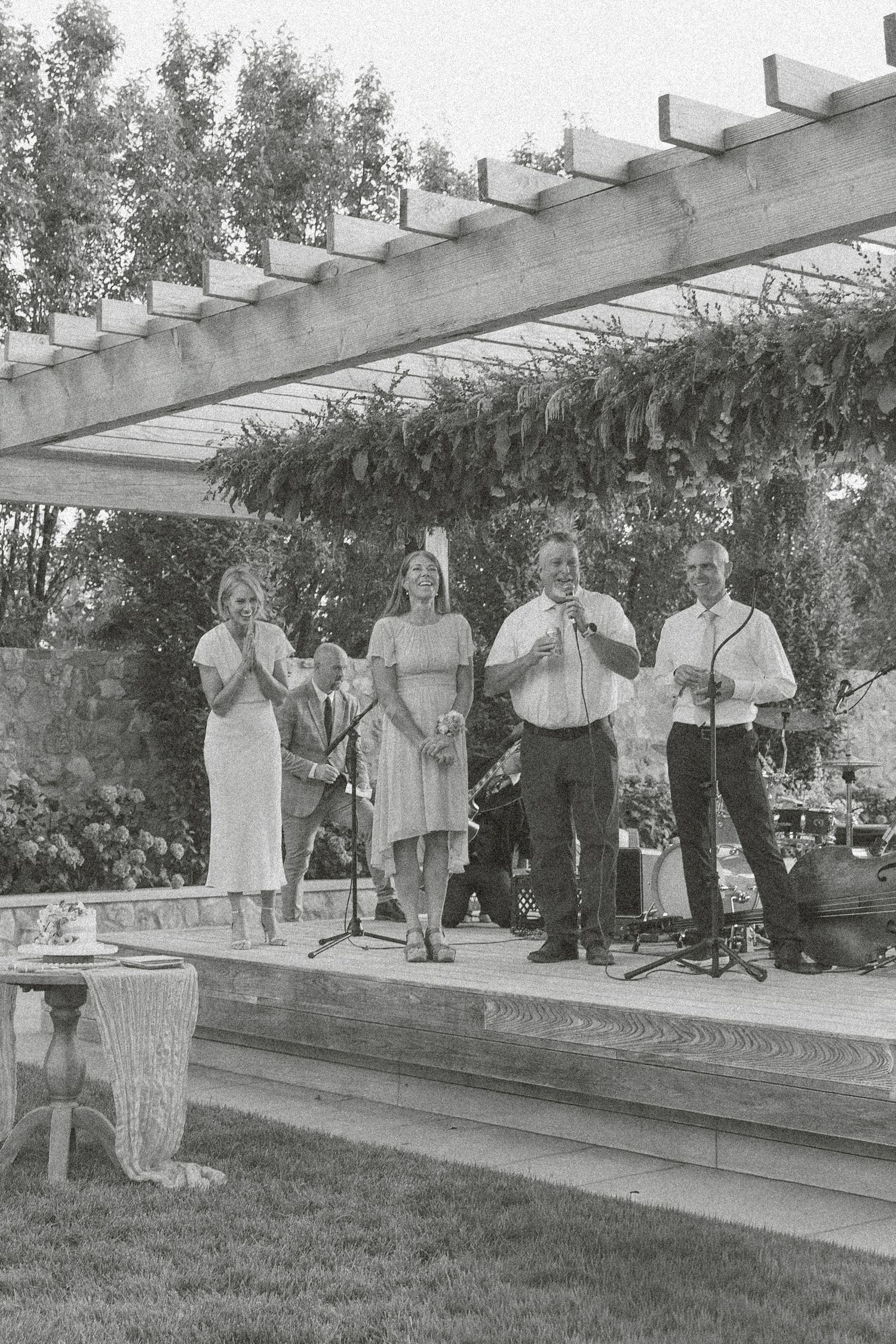 Black and white photo of wedding guests lined up under a wooden pergola structure.