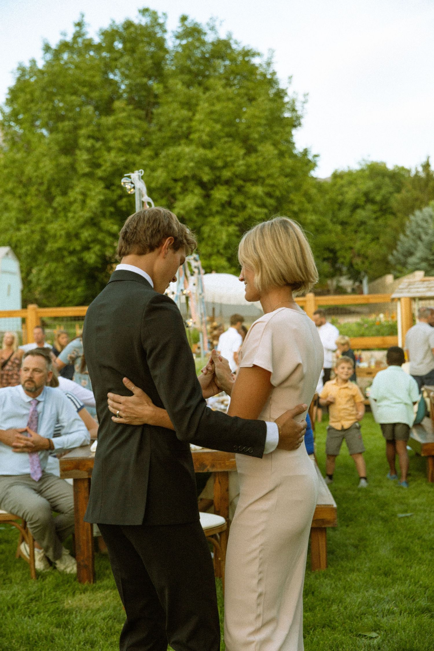 Couples dancing together on a grassy lawn during an outdoor wedding reception.