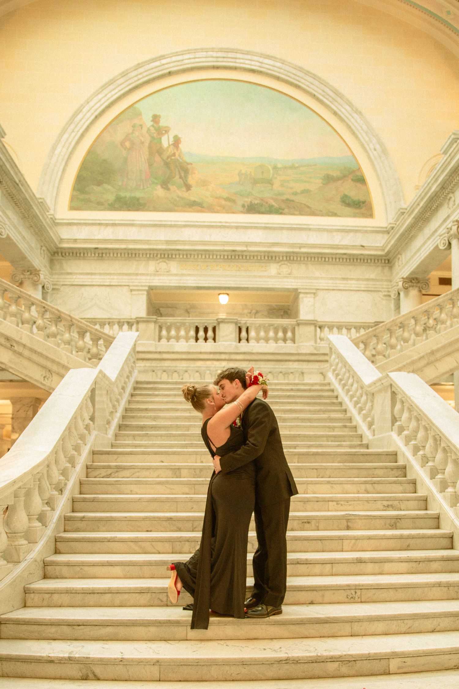A romantic embrace on an elegant marble staircase with arched ceiling and classical architecture in warm lighting.