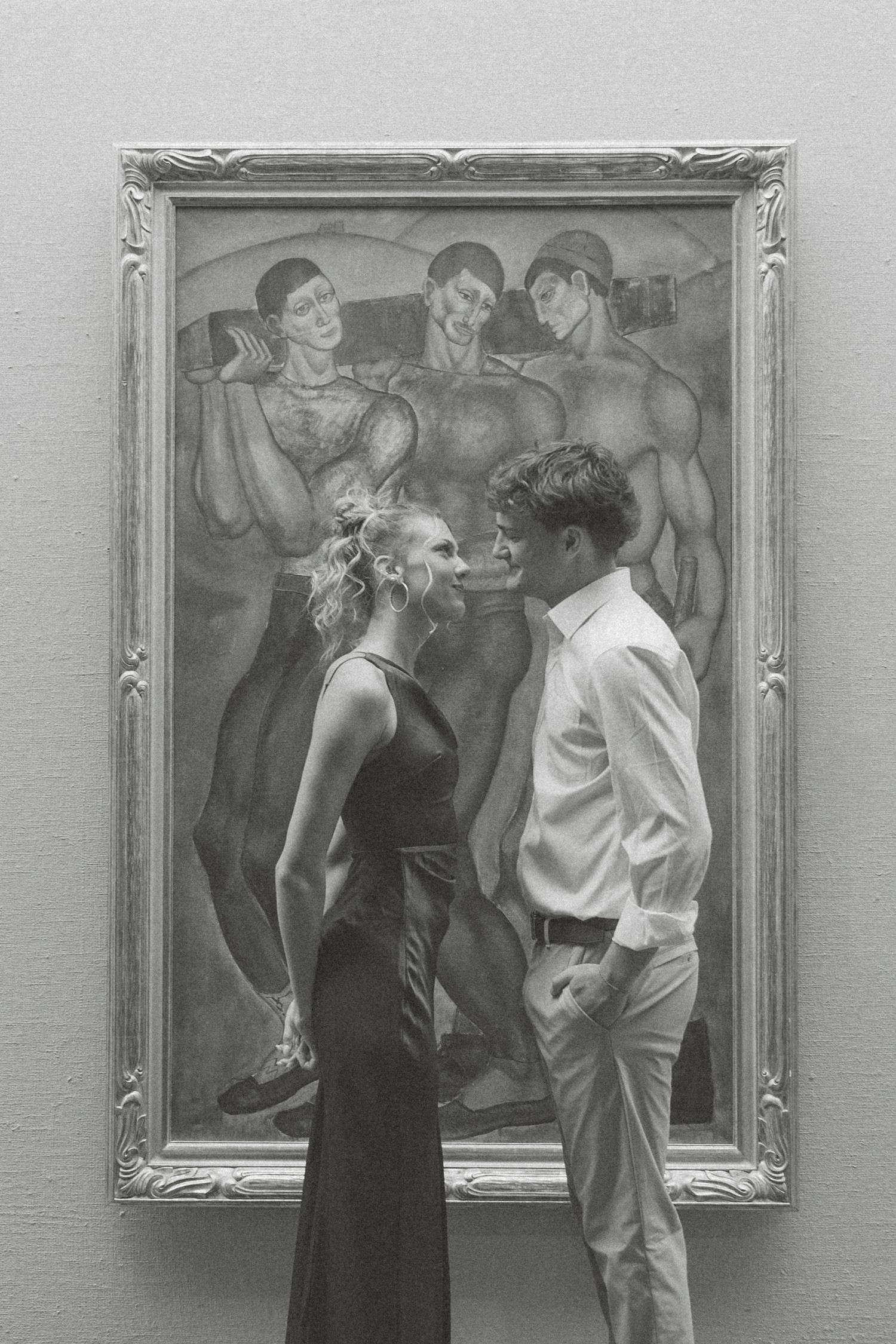 A couple in formal attire views and discusses artwork together at a gallery exhibition.
