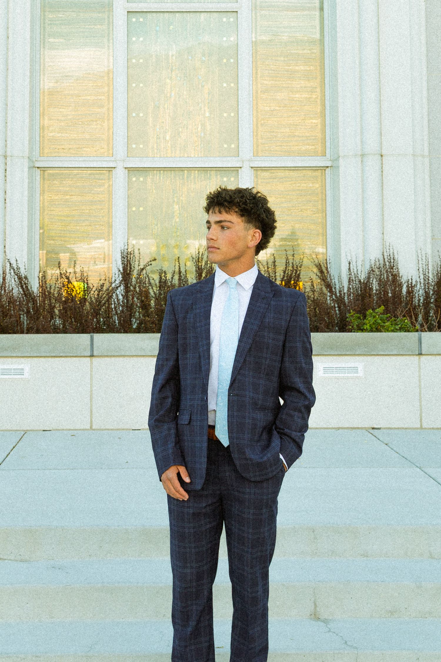 Young man in navy plaid suit standing confidently on steps outside a modern building.
