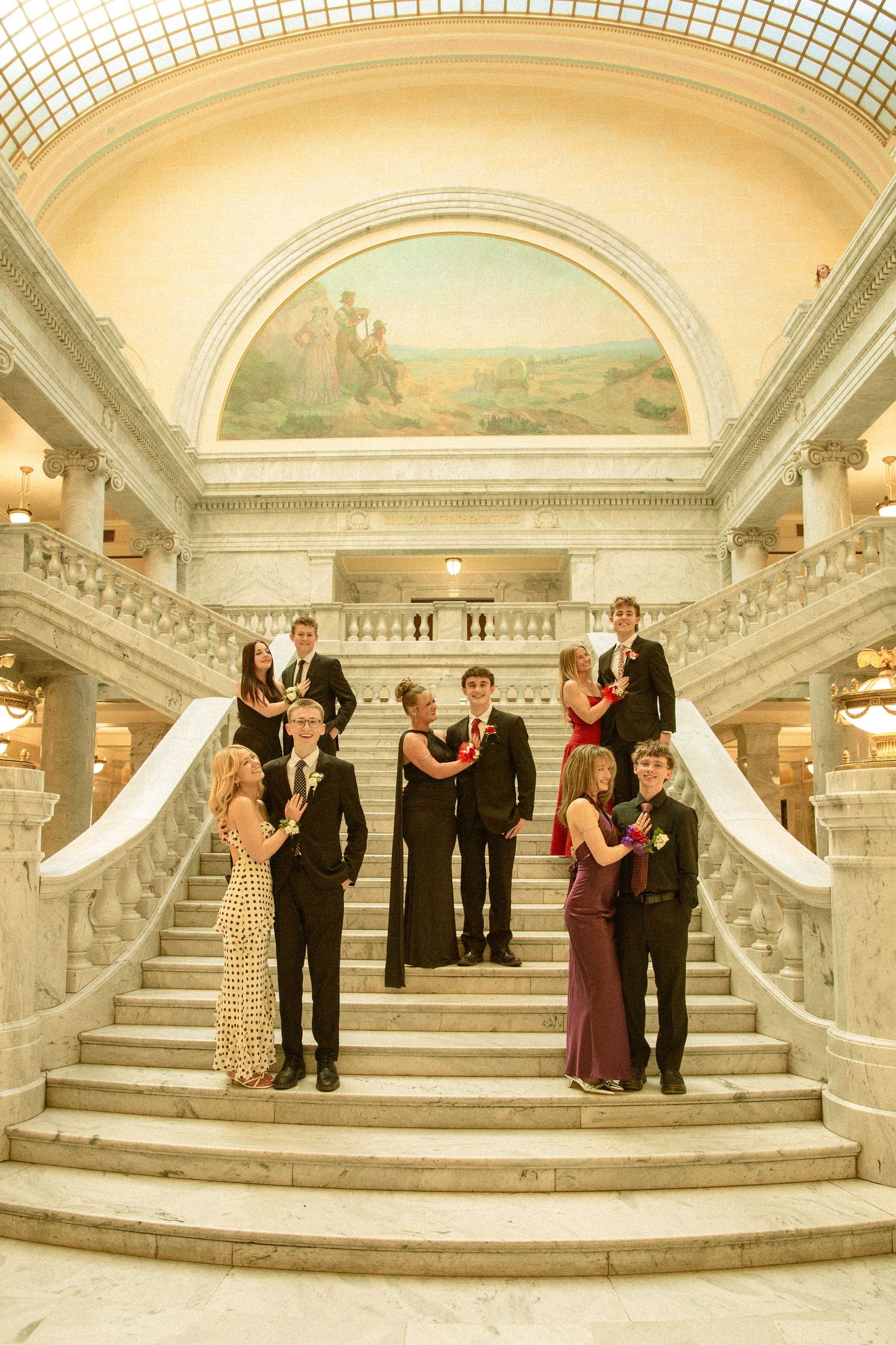 Formal group poses on elegant marble staircase with arched ceiling and mural in grand historic building interior.