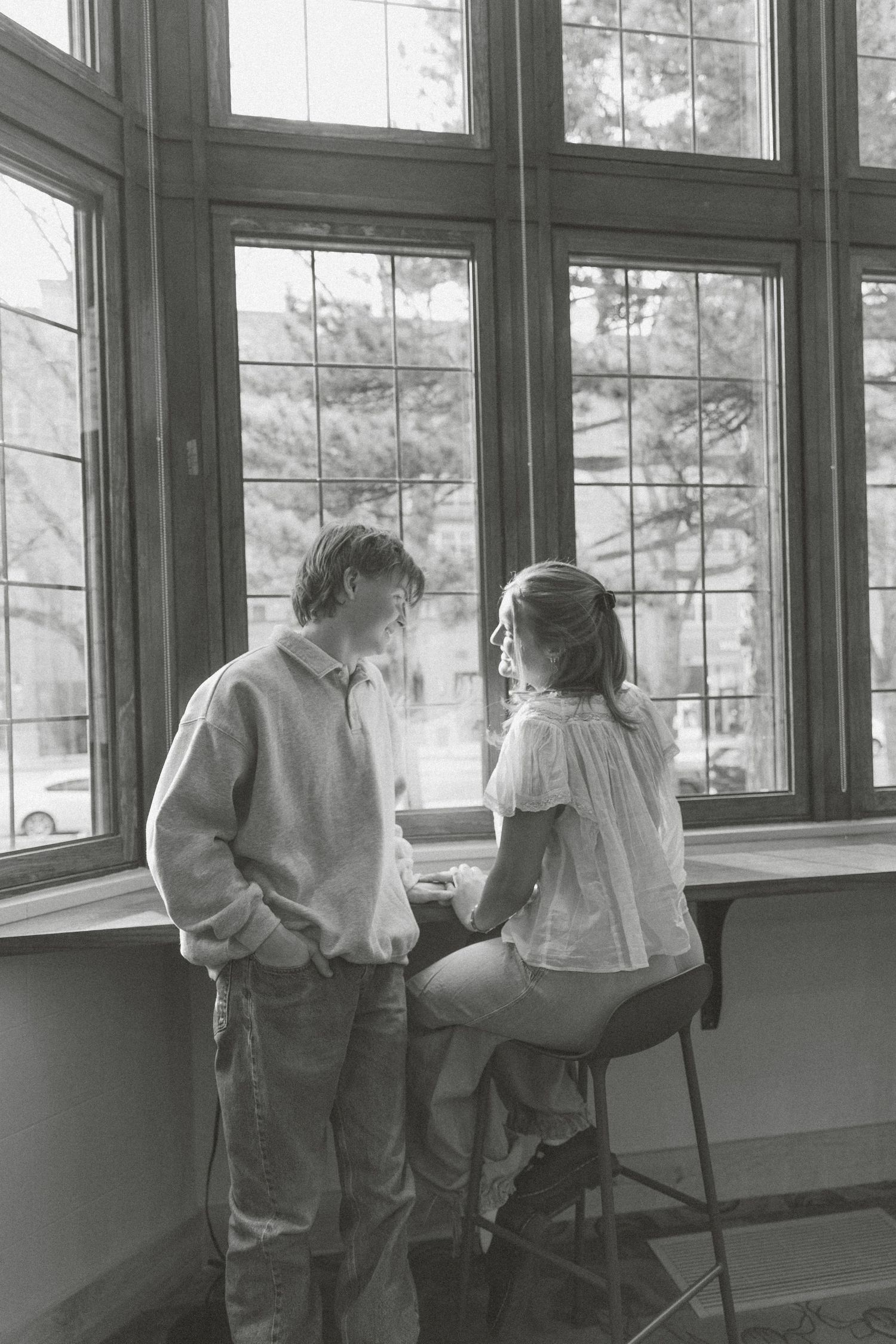 A black and white photo shows people looking out large windows in a sunlit interior space.