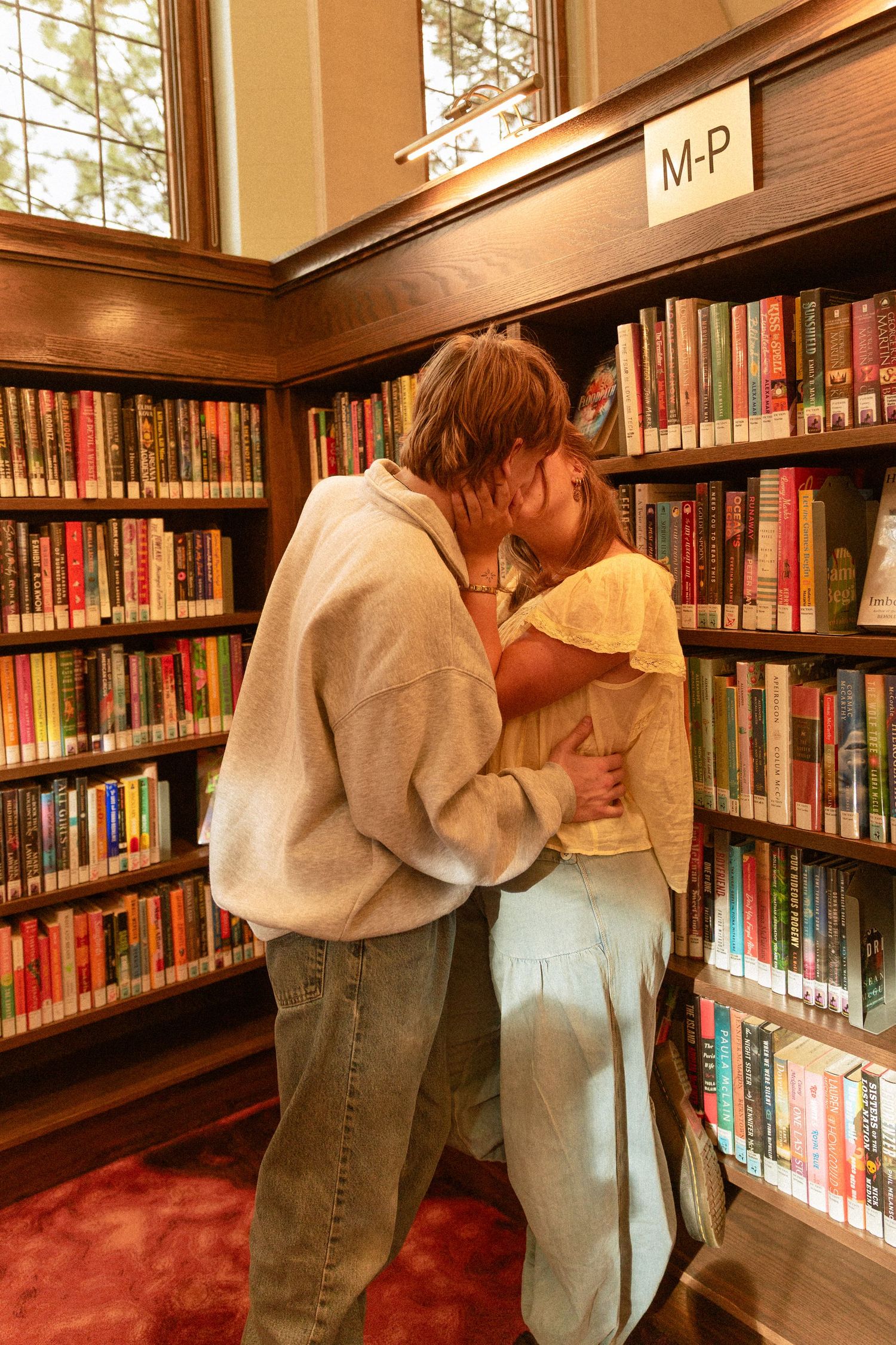 A couple shares an intimate moment between bookshelves in a library with warm lighting and wooden details.